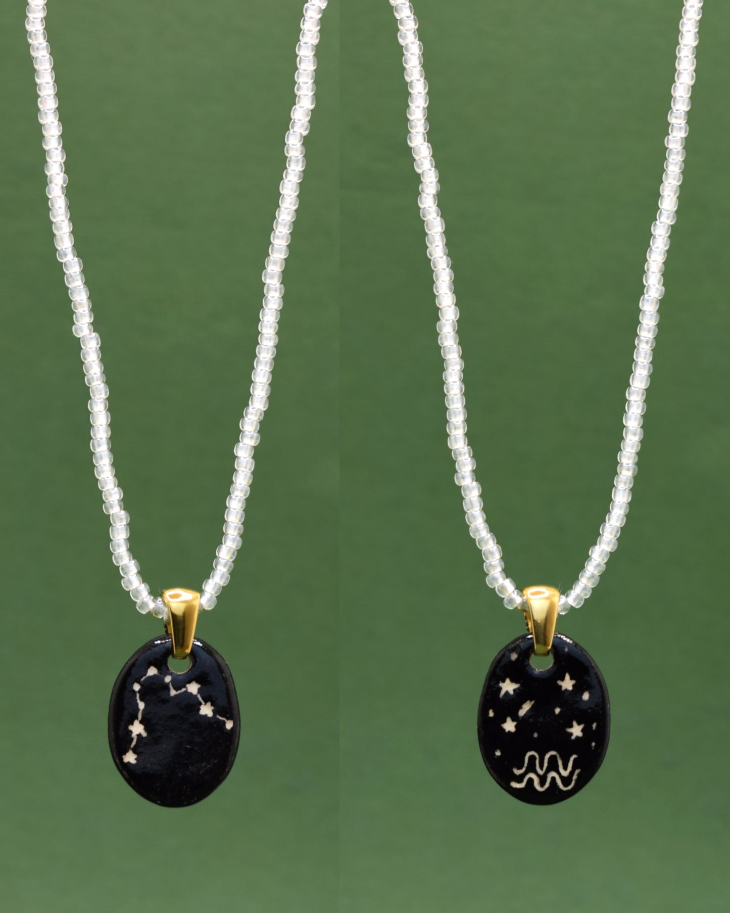Colar refinado apresentando um pendente dupla-face esculpido em cerâmica, destacando a constelação de Aquário, harmonizado com uma delicada corrente de missangas semitransparentes em branco para um toque de elegância etérea.