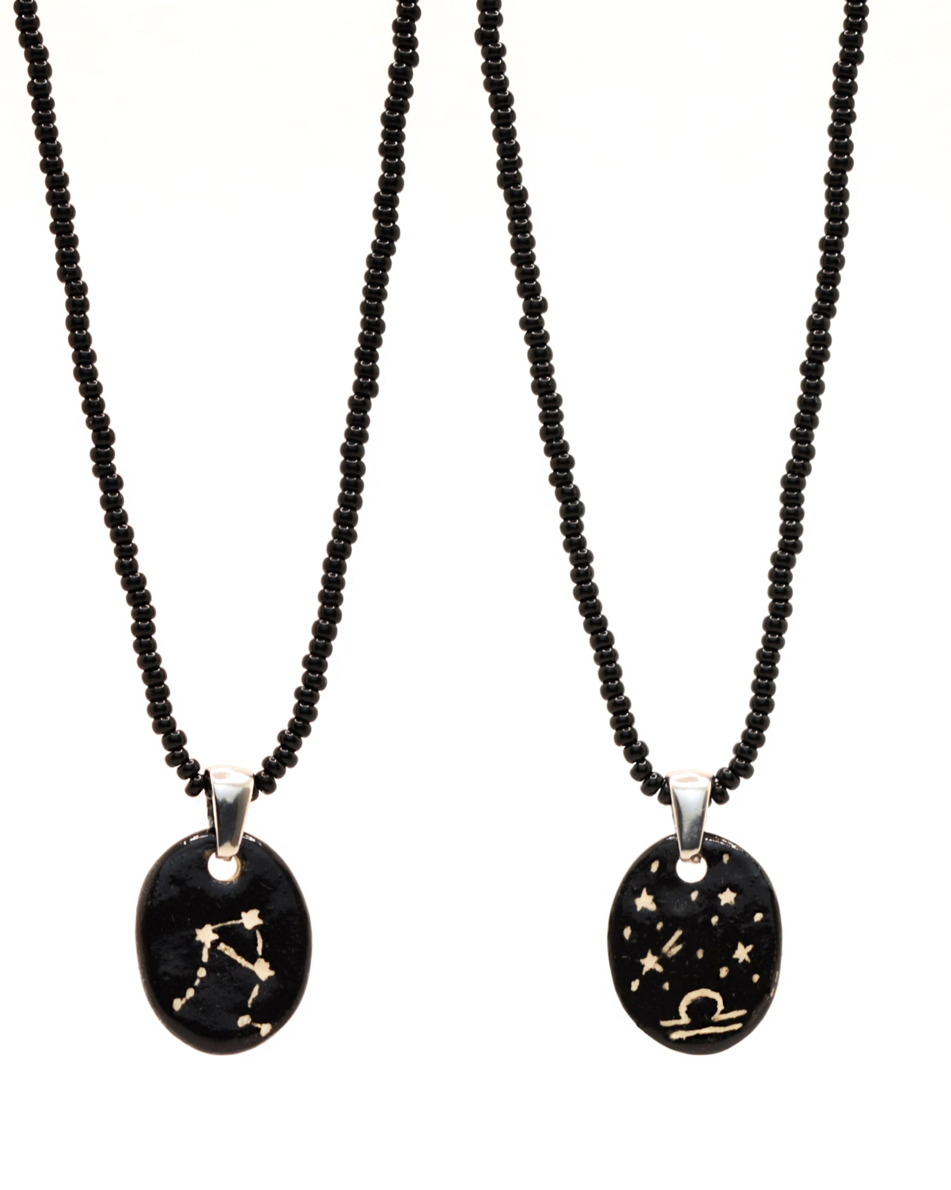 Colar elegante com pendente de cerâmica dupla-face representando a constelação Balança, adornado com missangas de vidro pretas para um toque sofisticado e misterioso.
