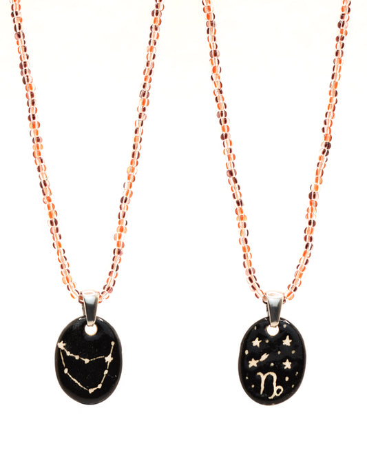 Colar elegante com pendente dupla-face esculpido em cerâmica, retratando a constelação de Capricórnio, complementado por missangas listradas em tons castanhos para um toque de estilo e charme distintos.