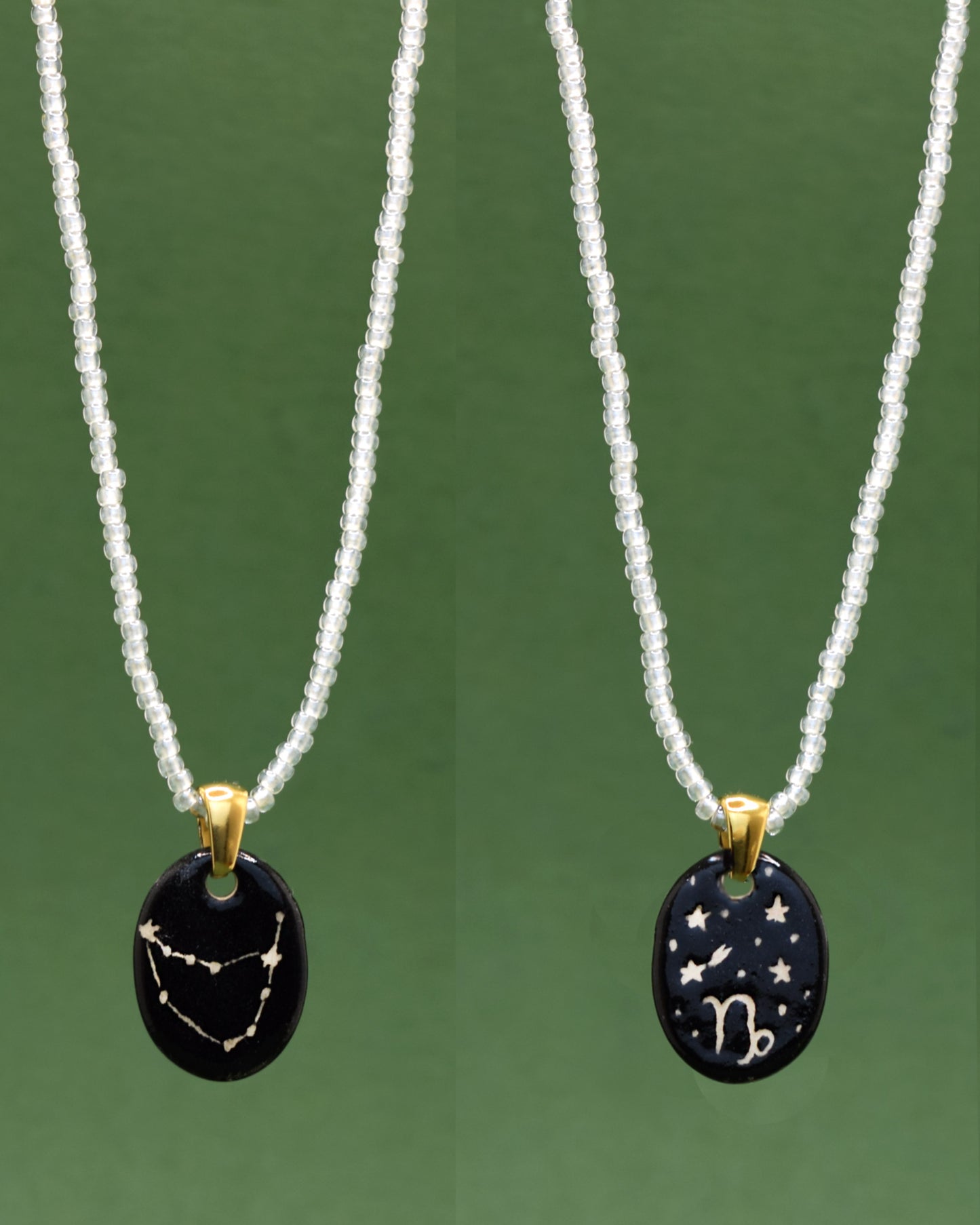 Colar refinado apresentando um pendente dupla-face esculpido em cerâmica, destacando a constelação de Capricórnio, harmonizado com uma delicada corrente de missangas semitransparentes em branco para um toque de elegância etérea.