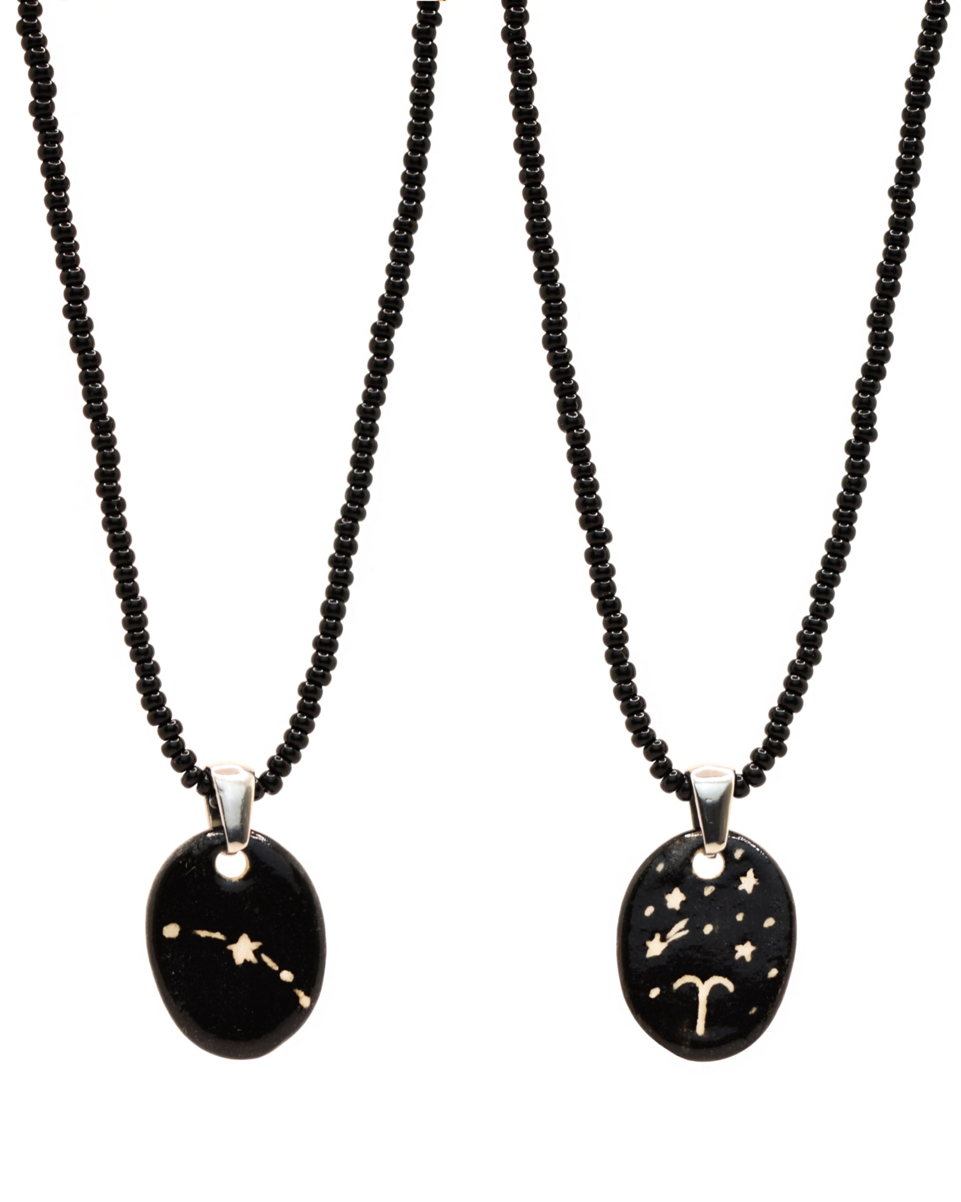 Colar elegante com pendente de cerâmica dupla-face representando a constelação Carneiro, adornado com missangas de vidro pretas para um toque sofisticado e misterioso.