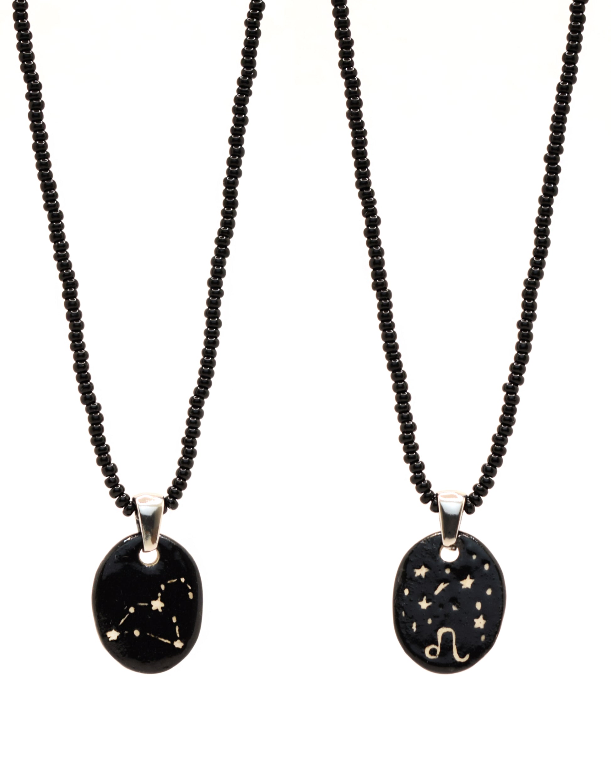 Colar elegante com pendente de cerâmica dupla-face representando a constelação Leão, adornado com missangas de vidro pretas para um toque sofisticado e misterioso.