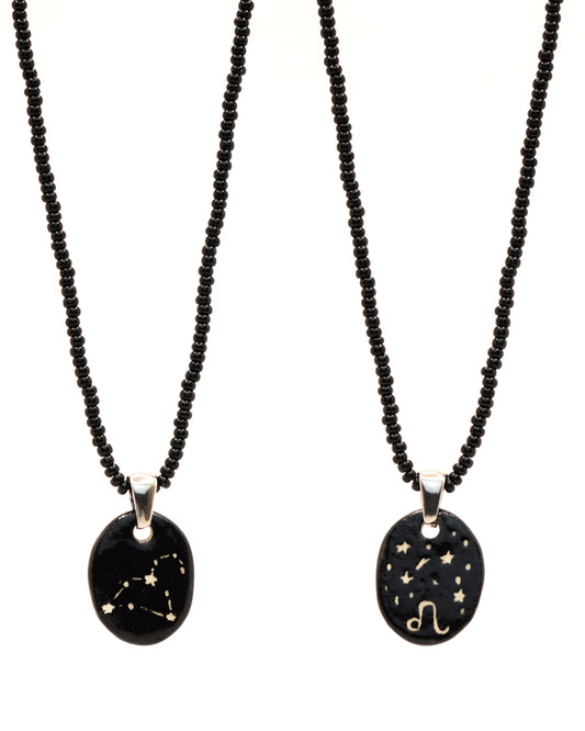 Colar elegante com pendente de cerâmica dupla-face representando a constelação Leão, adornado com missangas de vidro pretas para um toque sofisticado e misterioso.