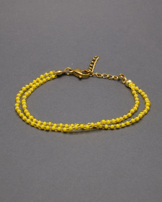 Pulseira dupla com missangas douradas semitransparentes e padrão amarelo. Design artesanal elegante para um look sofisticado.
