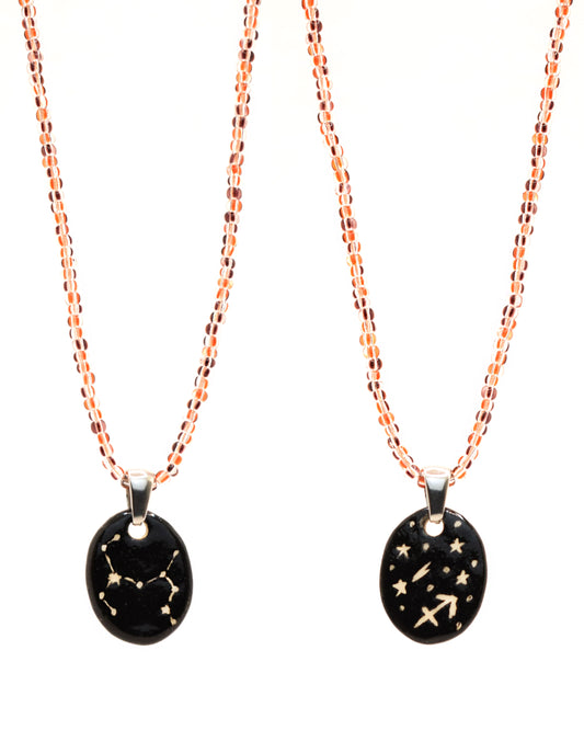 Colar elegante com pendente dupla-face esculpido em cerâmica, retratando a constelação de Sagitário, complementado por missangas listradas em tons castanhos para um toque de estilo e charme distintos.