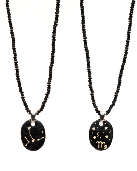 Colar elegante com pendente de cerâmica dupla-face representando a constelação Virgem, adornado com missangas de vidro pretas para um toque sofisticado e misterioso.