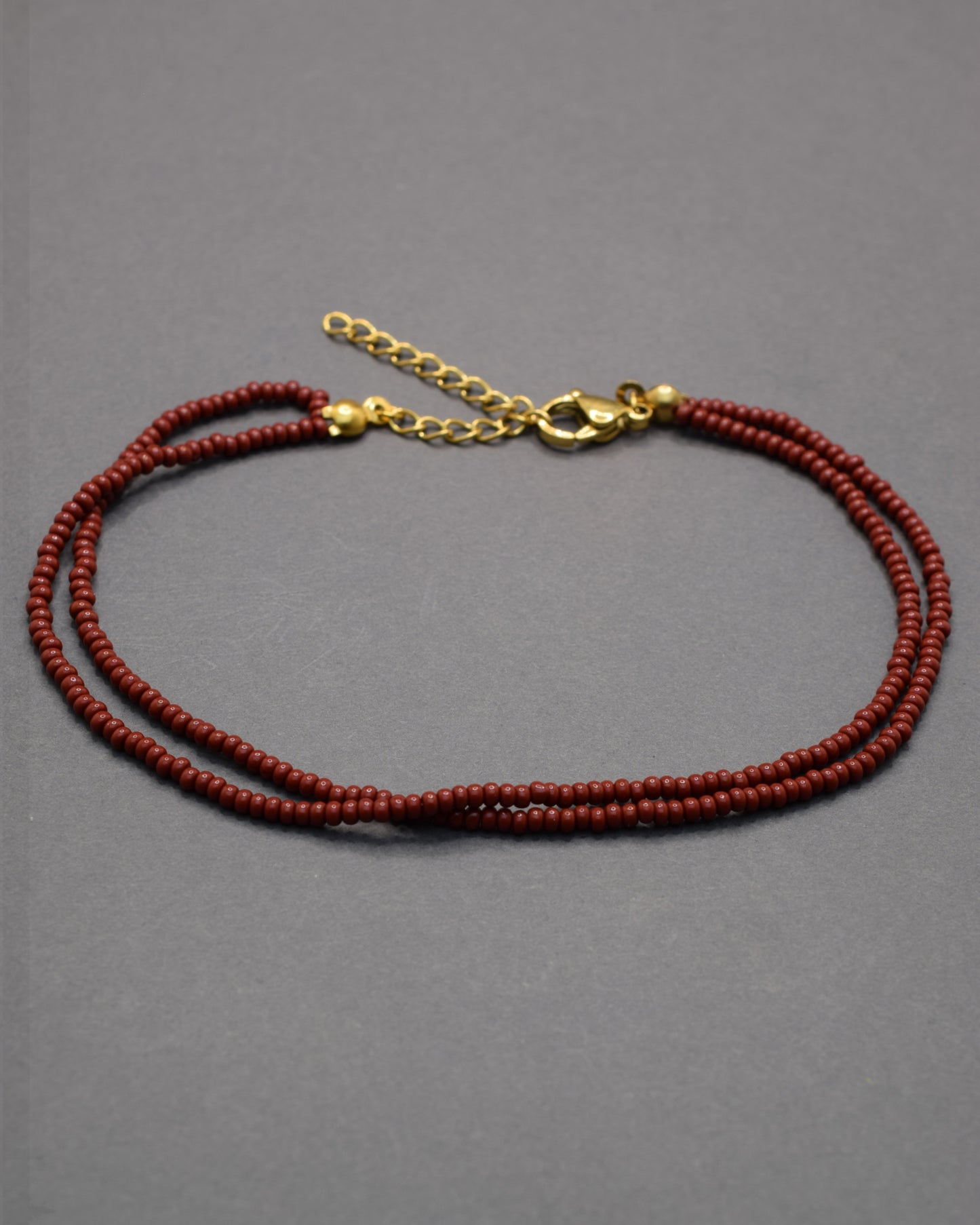 Pulseira dupla de tornozelo em missangas bordô, elegante e intensa, perfeita para um toque sofisticado e moderno no teu look.