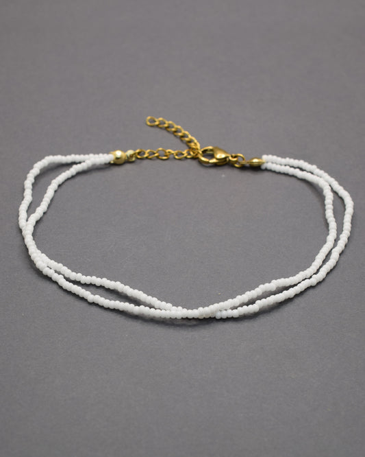 Pulseira dupla de tornozelo em missangas brancas, delicada e luminosa, perfeita para um look fresco, elegante e versátil em qualquer ocasião.