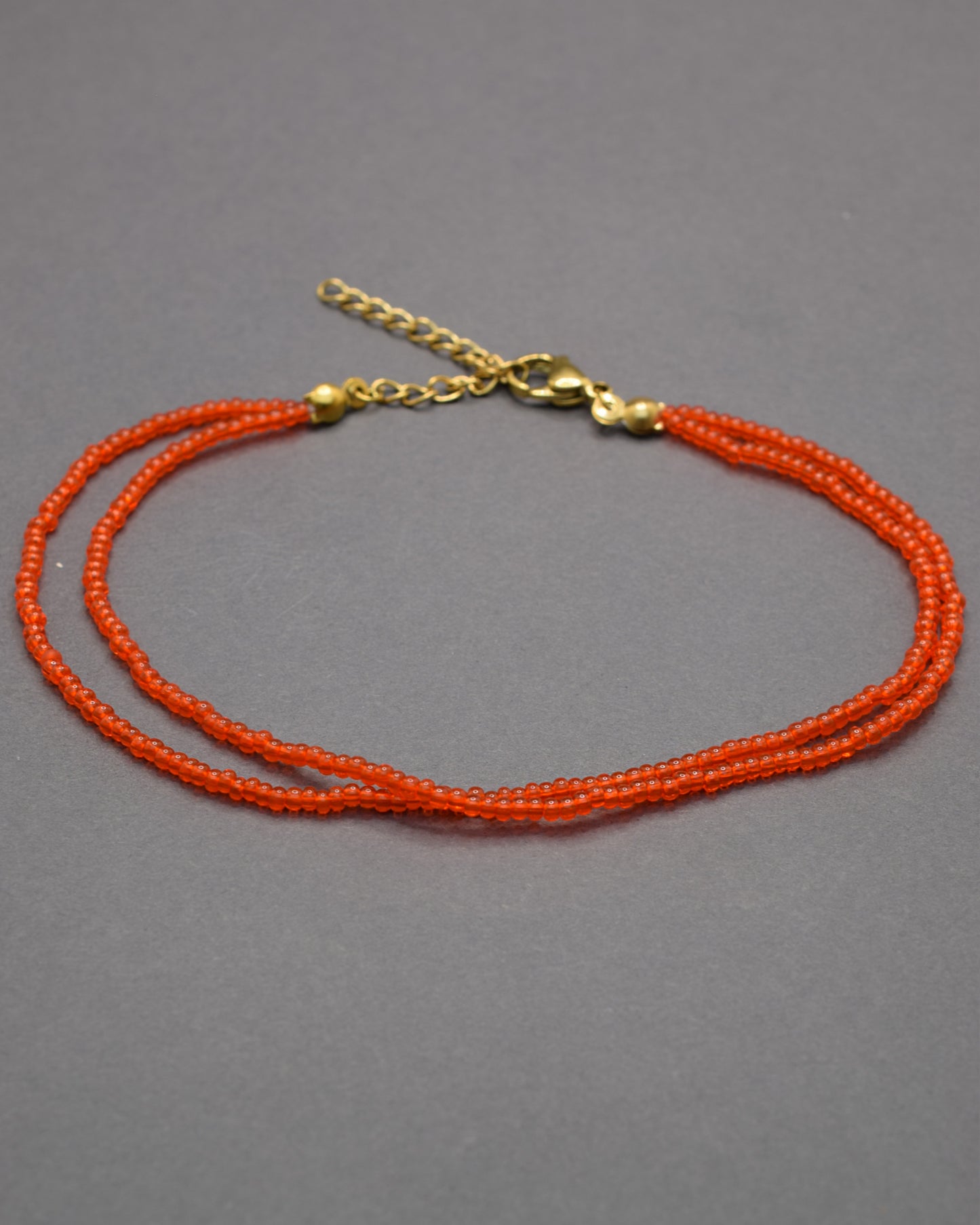 Pulseira dupla de tornozelo com missangas vermelhas-alaranjadas semitransparentes, vibrante e luminosa, perfeita para destacar o teu estilo.