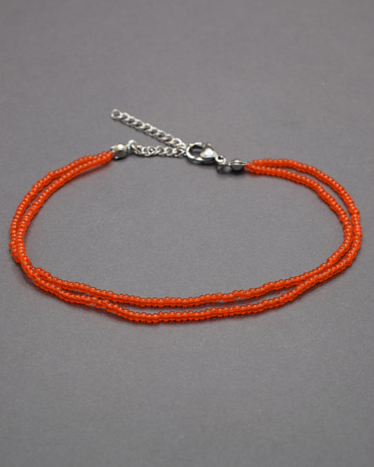 Pulseira dupla de tornozelo com missangas vermelhas-alaranjadas semitransparentes, vibrante e luminosa, perfeita para destacar o teu estilo.
