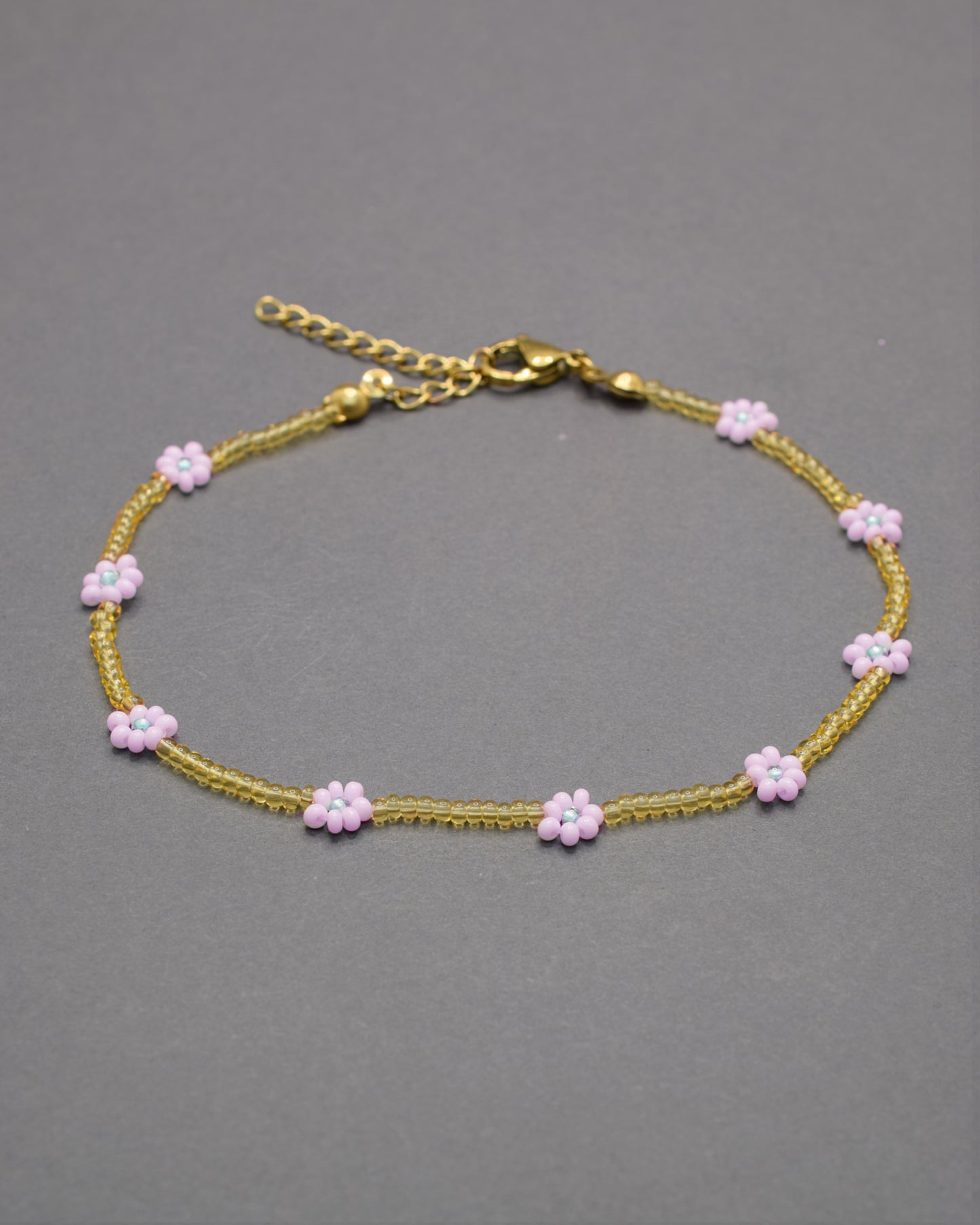Pulseira de tornozelo com flores rosa-claro e missangas douradas semitransparentes, delicada e elegante, perfeita para um toque romântico.