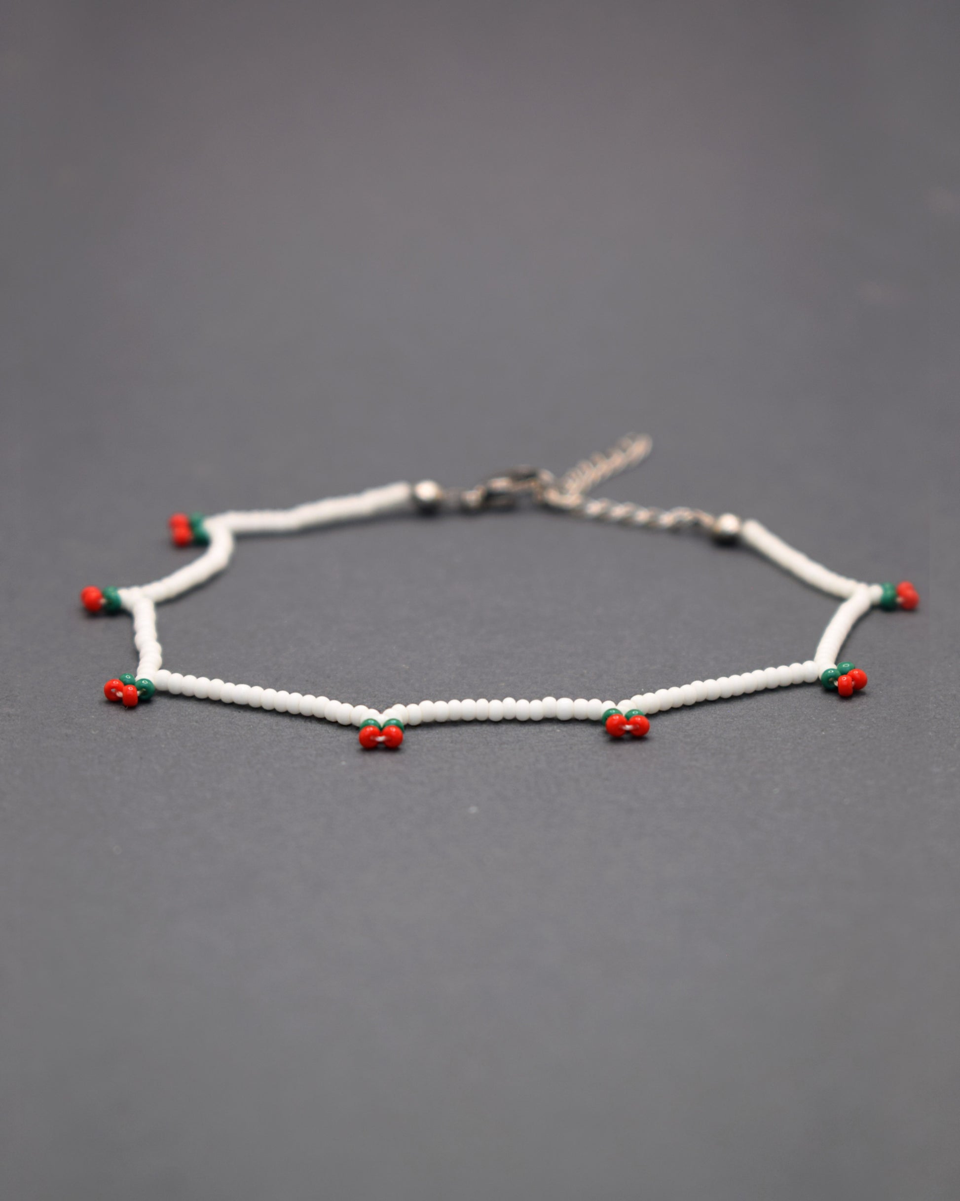Delicie-se com a nossa Pulseira de Pé Cerejas de Missangas, uma joia artesanal feita em missangas de vidro que celebra a frescura do verão. Com um delicado bordado de cerejas vibrantes, esta pulseira é adornada com fecho em aço inoxidável hipoalergénico.