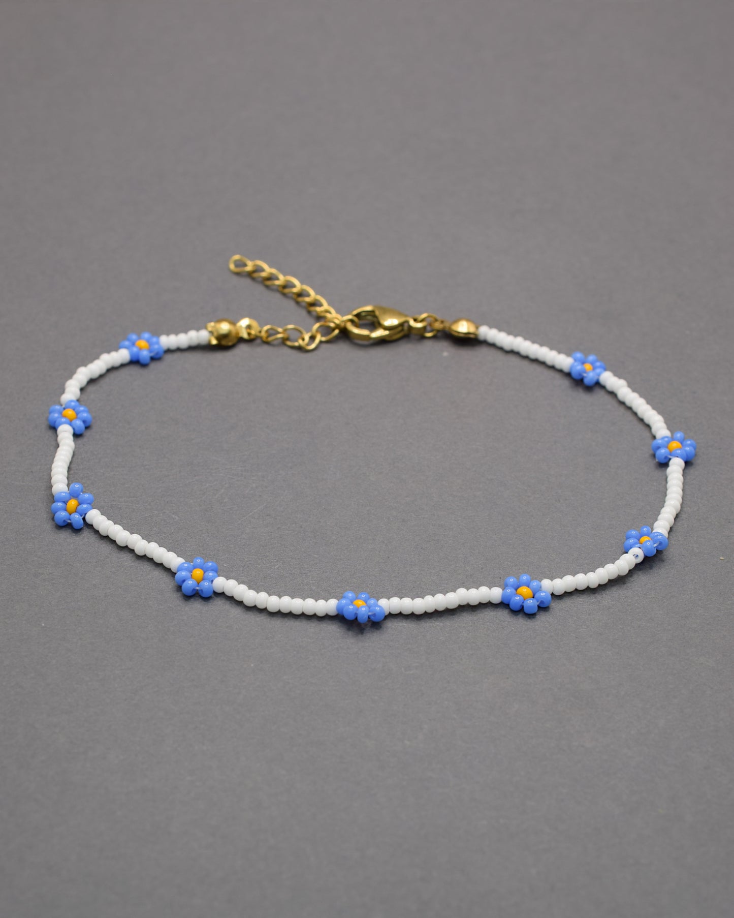 Pulseira de tornozelo em missangas brancas com flores azuis. Delicada e leve, perfeita para um toque fresco e elegante no dia a dia.
