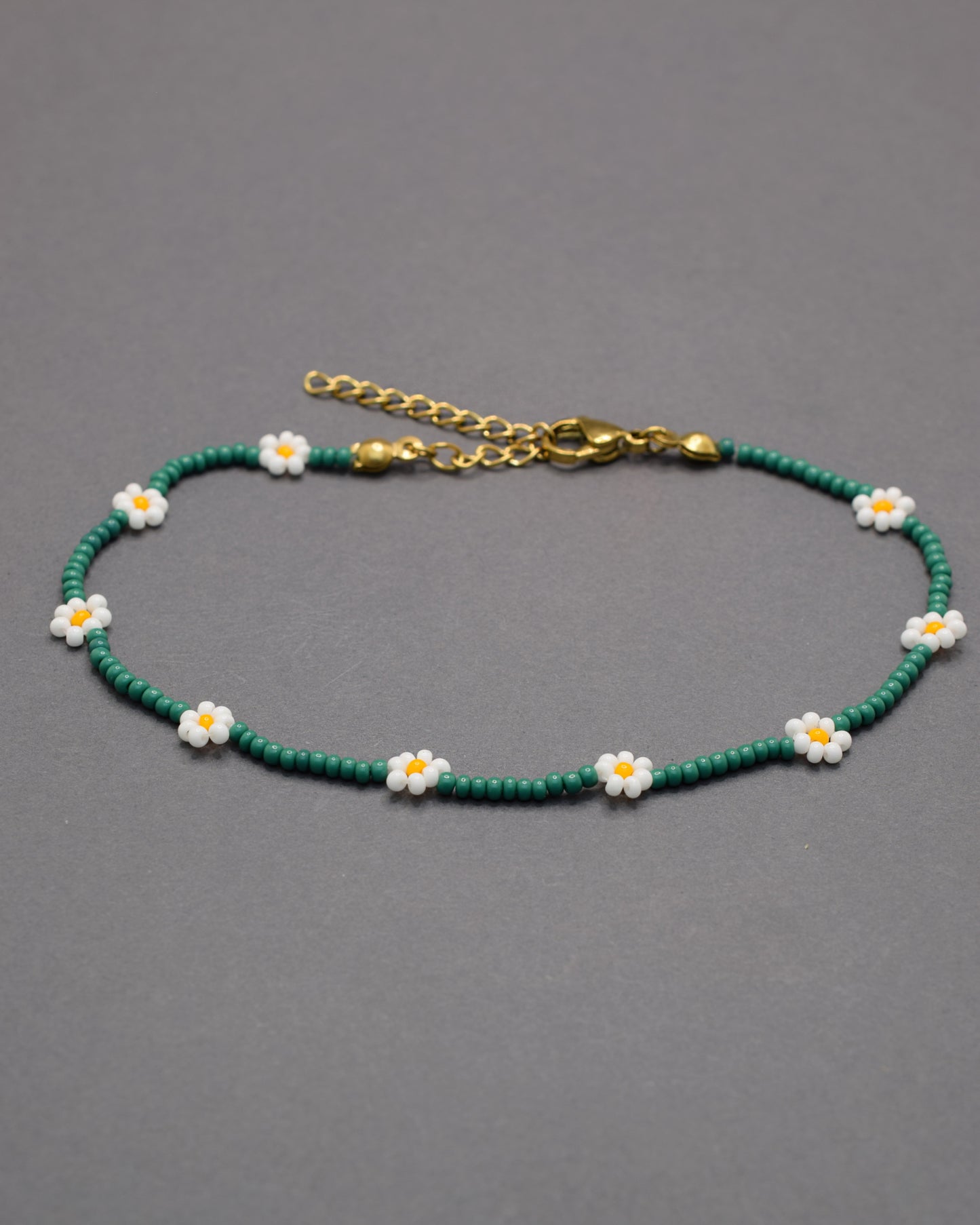 Pulseira de tornozelo em missangas verdes com flores brancas. Leve e fresca, ideal para um toque natural e delicado no teu estilo.
