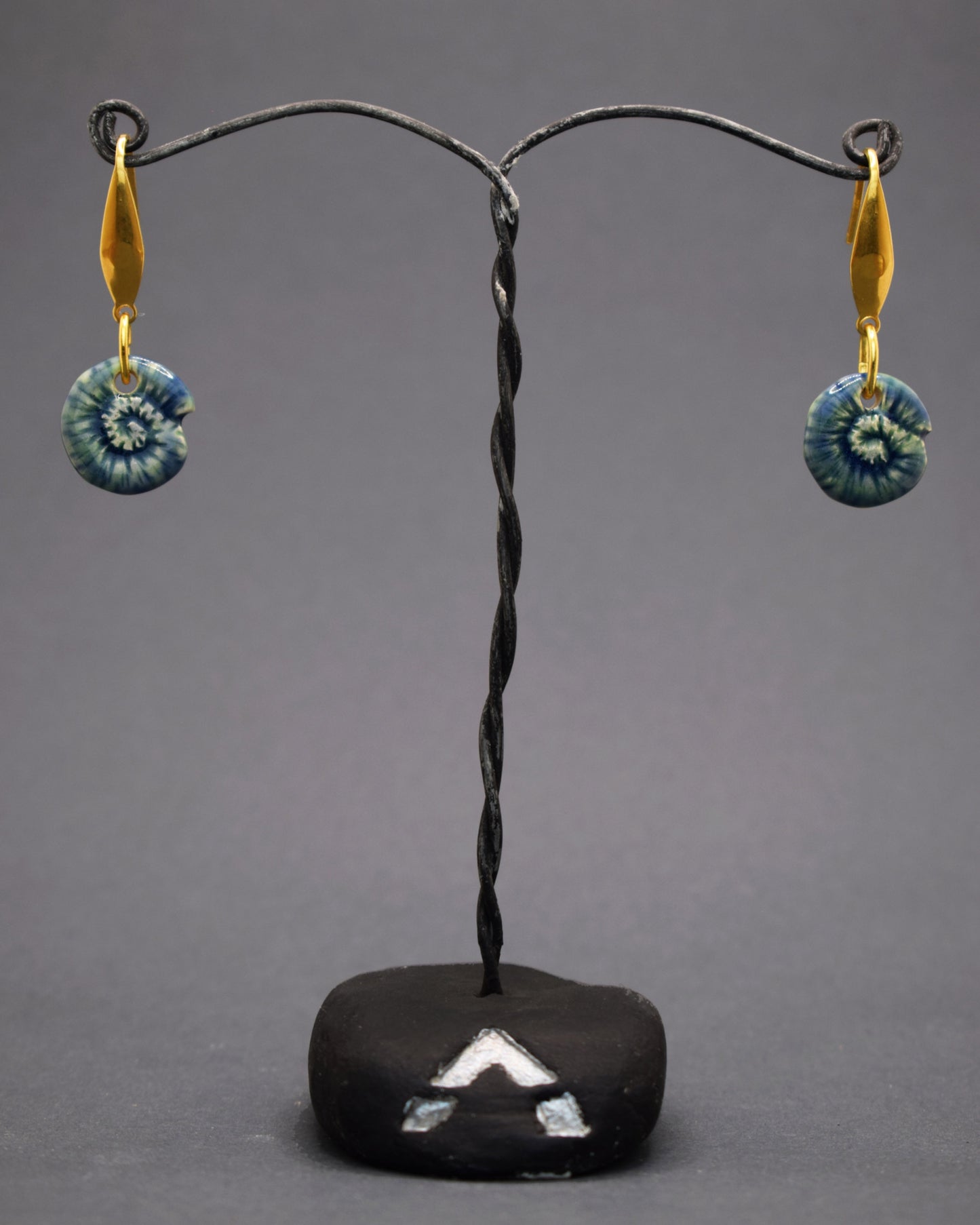 Adicione um toque natural ao seu estilo com brincos de aço inoxidável dourado, cada um com um pendente de cerâmica feito e pintado à mão, exibindo um caracol verde musgo. Uma combinação única de arte e natureza para um visual encantador.