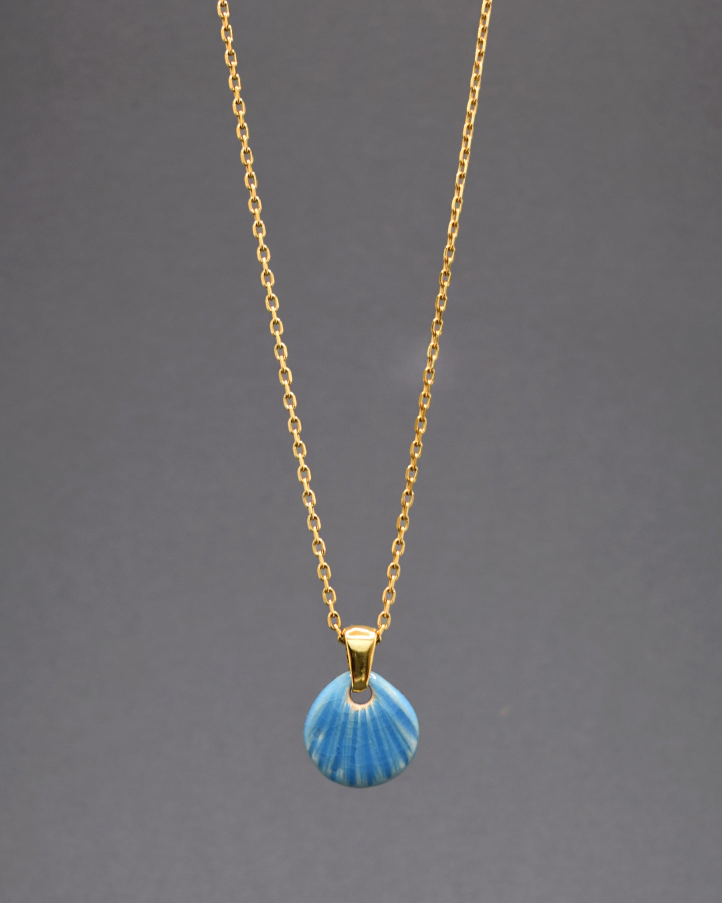 Descubra a elegância deste colar em aço inoxidável dourado com um pendente de concha em cerâmica azul clara. Com um design delicado e artesanal, ele captura a beleza serena do oceano, adicionando um toque sofisticado e exclusivo ao seu visual. Perfeito para qualquer ocasião.