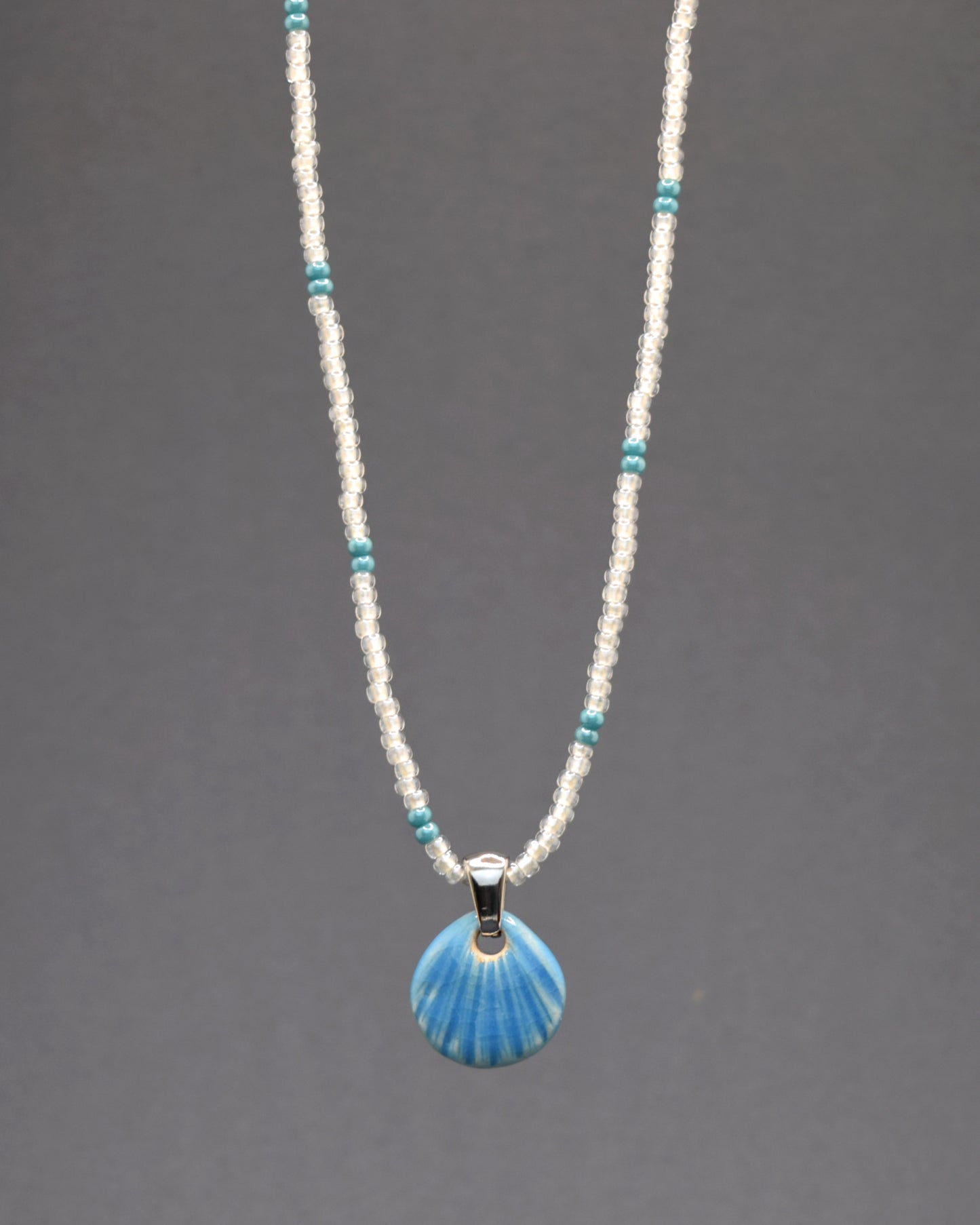 Descubra este colar de missangas de vidro brancas semitransparentes com padrão turquesa, acompanhado de um pendente de concha em cerâmica azul clara. Com um design artesanal e delicado, ele adiciona um toque de elegância e sofisticação ao seu visual, perfeito para qualquer ocasião.