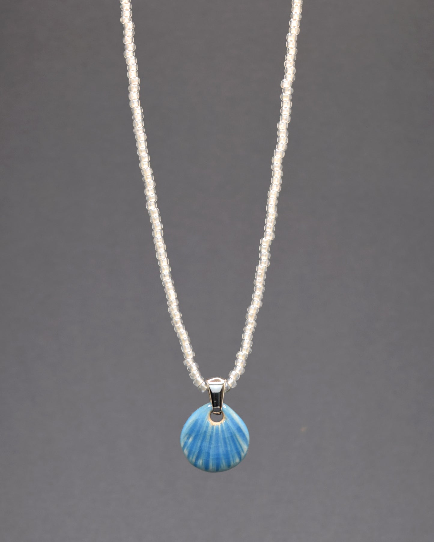 Encante-se com este colar de missangas de vidro brancas semitransparentes, adornado com um pendente de concha em cerâmica azul clara. Com um design delicado e artesanal, ele traz um toque de elegância serena e sofisticação ao seu visual. Perfeito para qualquer ocasião.