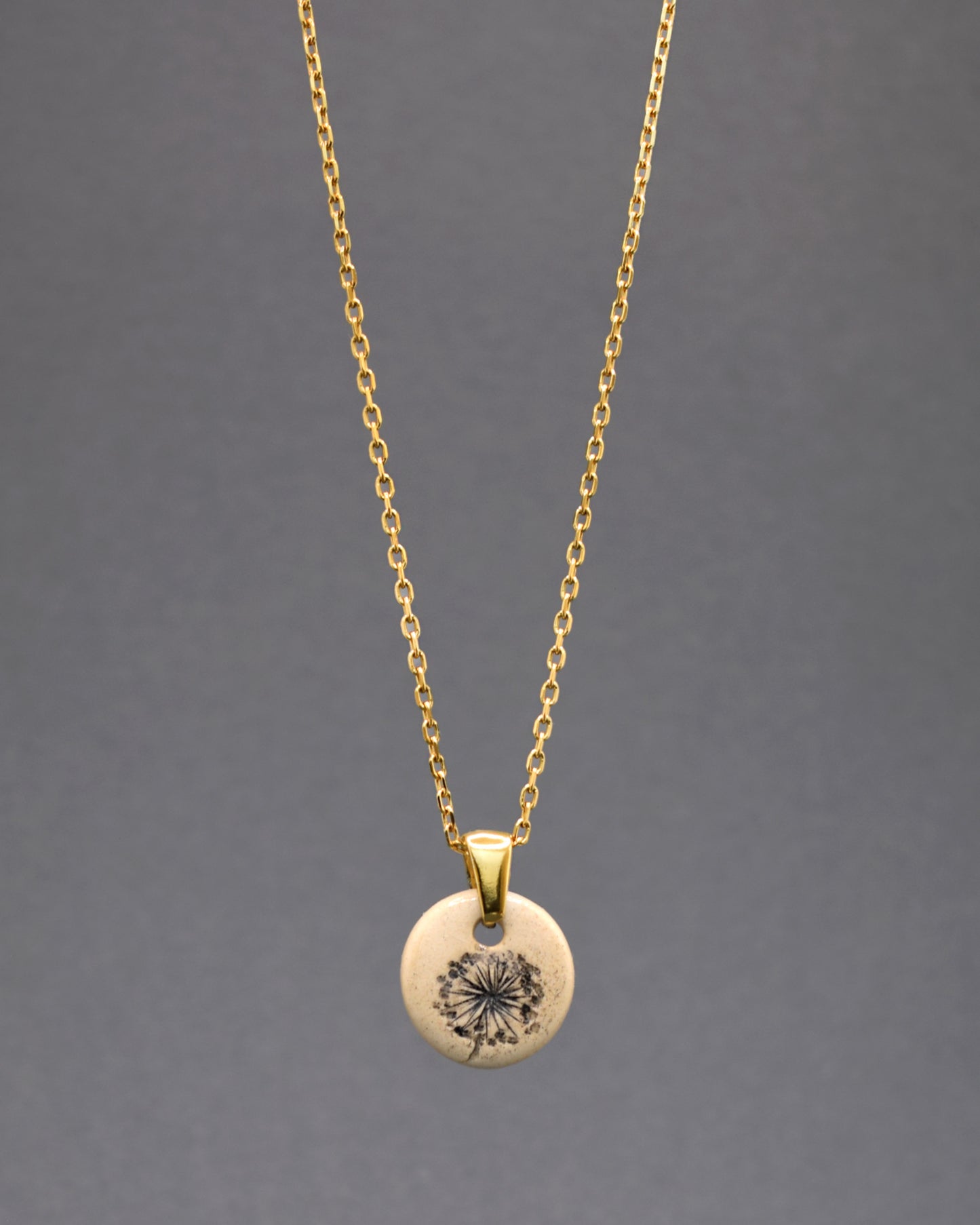 Este colar em aço inoxidável dourado, adornado com um pendente de cerâmica artesanal, captura a essência das plumas de dente de leão com delicadeza e precisão. A combinação do brilho dourado com a pureza do desenho oferece uma peça de joalheria única, simbolizando esperança e renovação. Ideal para adicionar um toque de elegância sutil e significativa ao seu estilo.