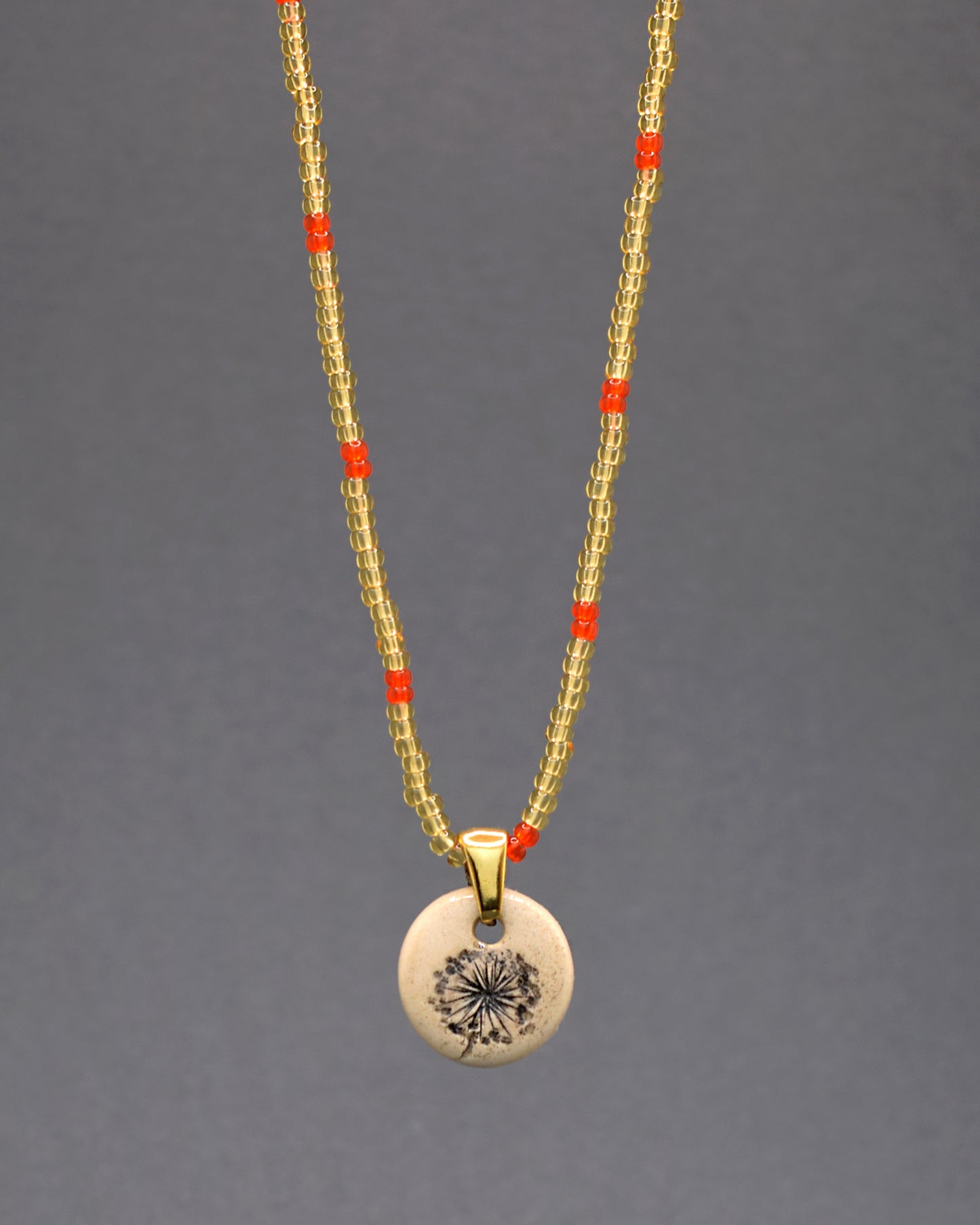 Explore a elegância com o nosso colar exclusivo de missangas douradas semitransparentes, adornado com um padrão vibrante em tons vermelho-alaranjado. O toque artesanal destaca-se no pendente de cerâmica, apresentando o encantador desenho de plumas de dente de leão. Uma fusão de cores e texturas que adicionam sofisticação e vitalidade ao seu estilo diário.
