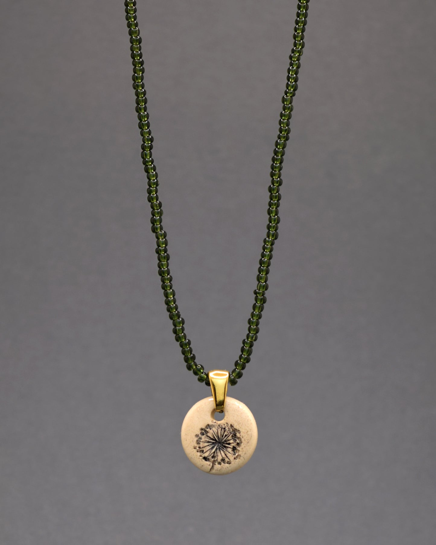 Encante-se com a serenidade da natureza neste colar único, com missangas de vidro verde-escuras semitransparentes. O pendente de cerâmica, habilmente trabalhado à mão, exibe o gracioso desenho das plumas de dente de leão. Uma fusão de tons naturais que eleva a sofisticação, proporcionando um toque de frescor e elegância ao seu visual diário.