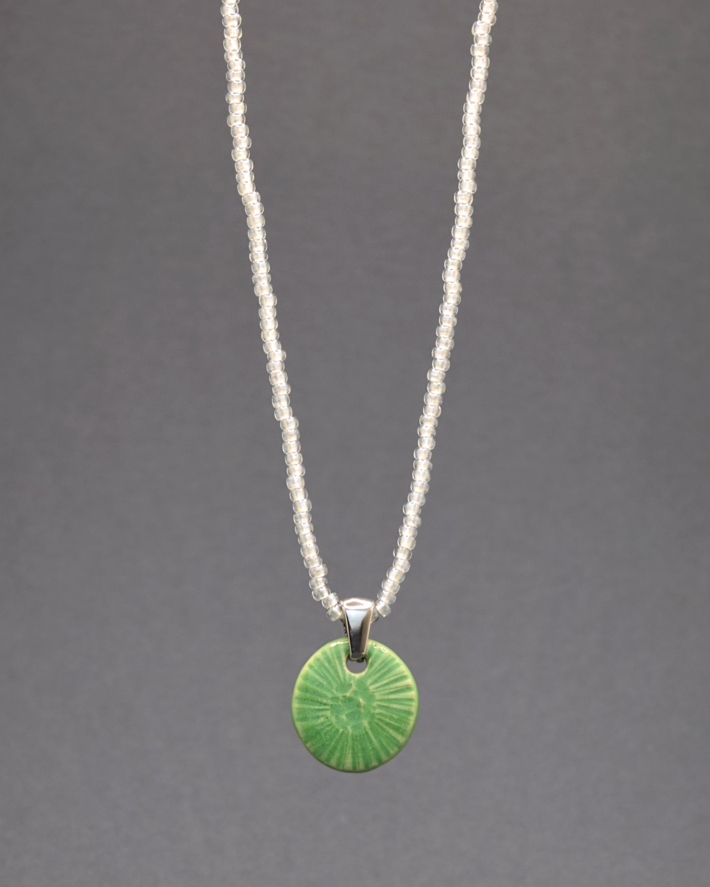 Este colar encantador apresenta um pendente de cerâmica feito à mão, inspirado na beleza sutil da flor do mar em um verde alface, delicadamente suspenso em uma corrente de missangas de vidro brancas semitransparentes. Uma peça única que combina a elegância artesanal da cerâmica com a delicadeza das missangas, criando um visual encantador e sofisticado.