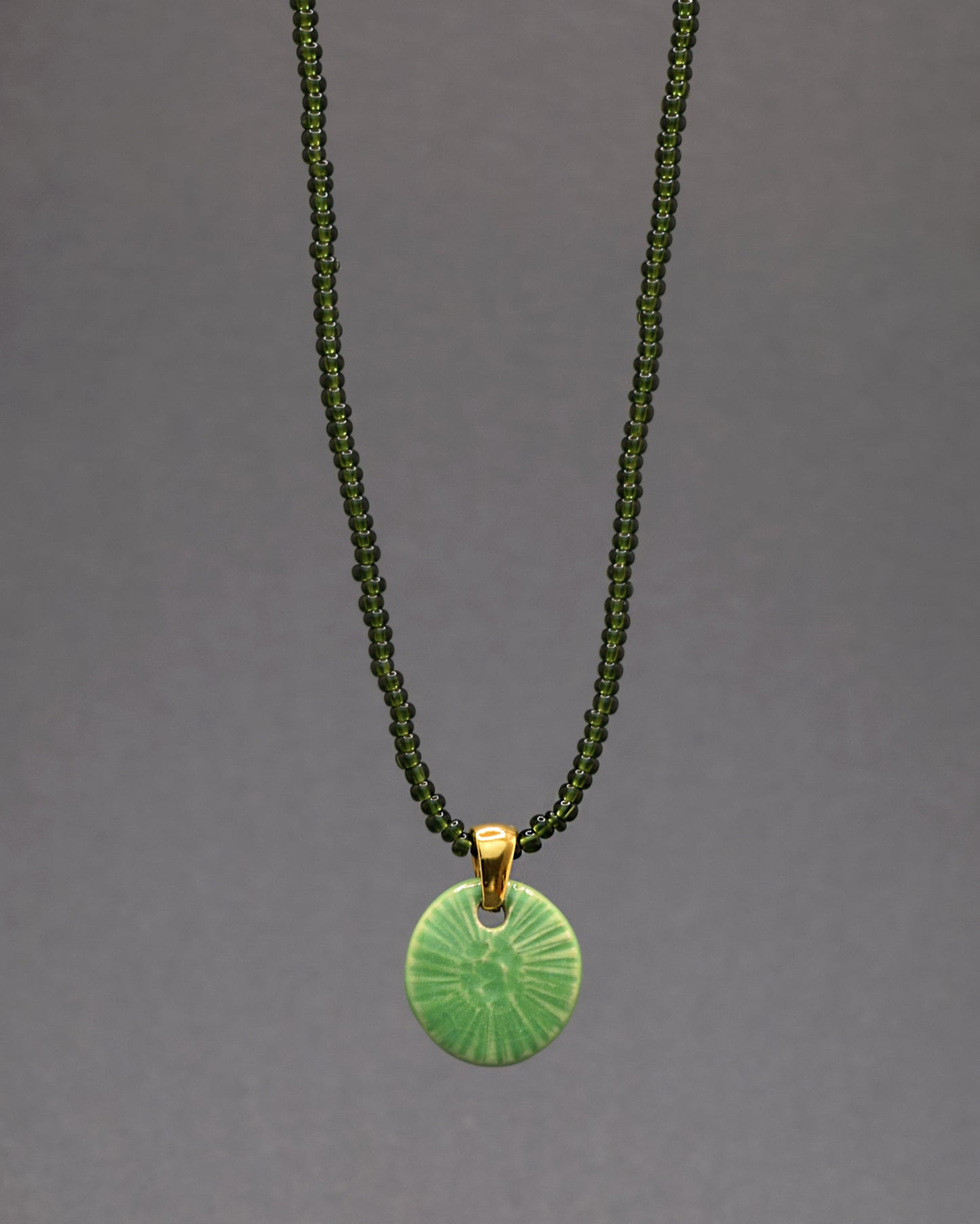 Este colar encantador apresenta um pendente de cerâmica feito à mão, inspirado na graciosidade da flor do mar em verde alface. Destacando-se em uma corrente de missangas de vidro verde escuro semitransparentes, a peça combina a elegância artesanal da cerâmica com a sofisticação das tonalidades profundas, resultando em uma joia única e estilizada.