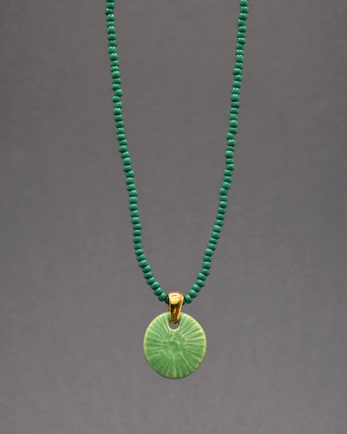 Este colar cativante apresenta um pendente de cerâmica feito à mão, evocando a beleza singular da flor do mar em verde alface. Suspenso em uma corrente de missangas de vidro verdes, cria uma peça encantadora que combina a delicadeza artesanal da cerâmica com a vivacidade das missangas, oferecendo um toque distintivo de elegância à sua joalheria.