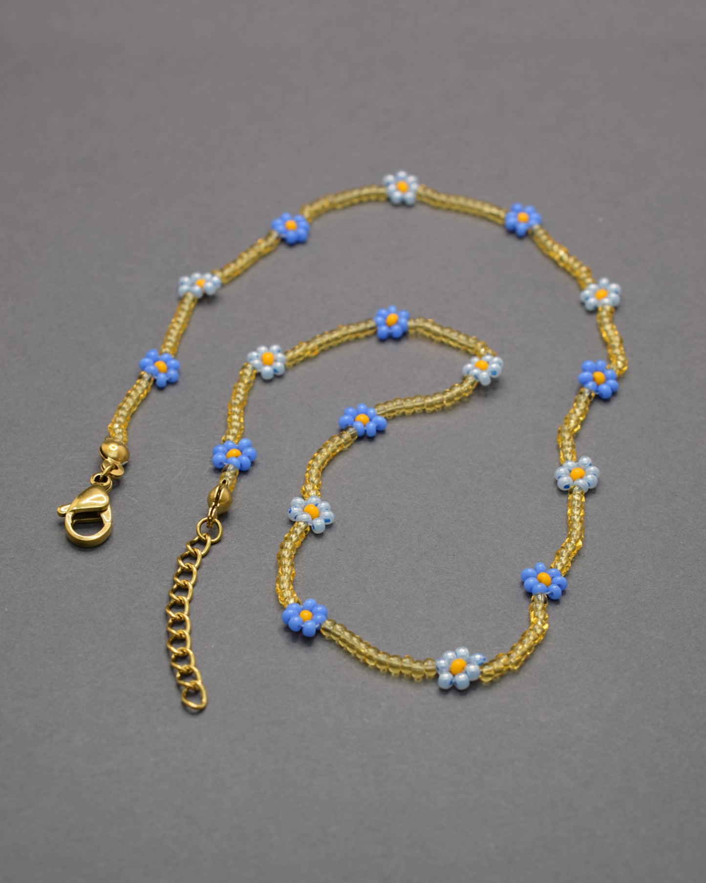 Colar com flores azul-claras e néon e missangas douradas semitransparentes, vibrante e delicado, perfeito para iluminar o teu estilo.