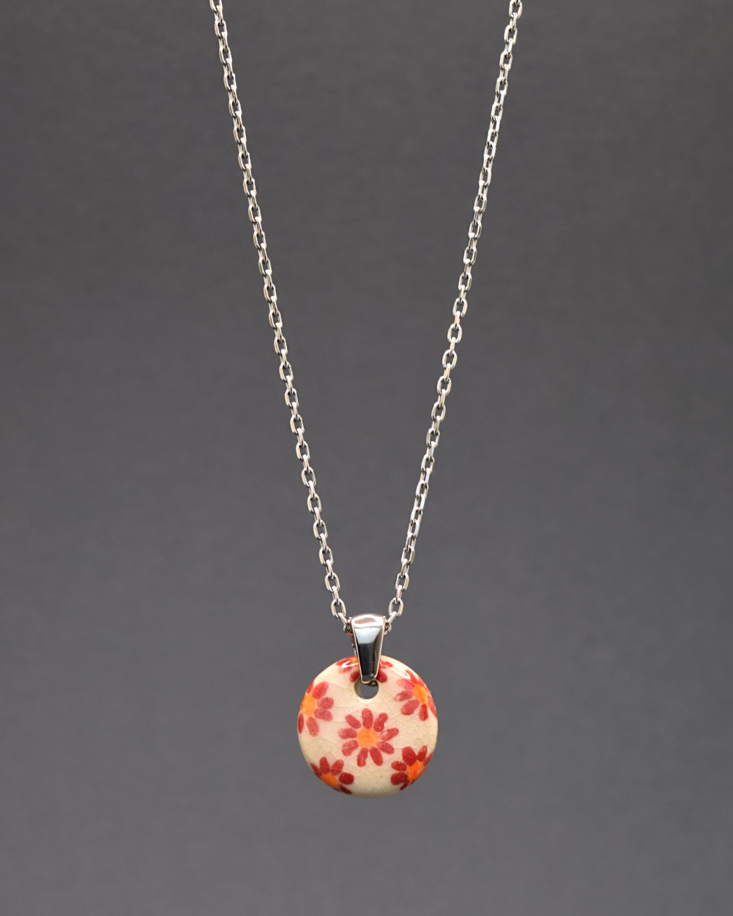 Explore a harmonia elegante entre o pendente de cerâmica com fundo branco e margaridas vermelhas, delicadamente suspenso em um colar de aço inoxidável. Uma fusão perfeita de design artesanal e modernidade, este colar cativa com sua sofisticação atemporal, adicionando um toque de frescor e beleza única ao seu visual.