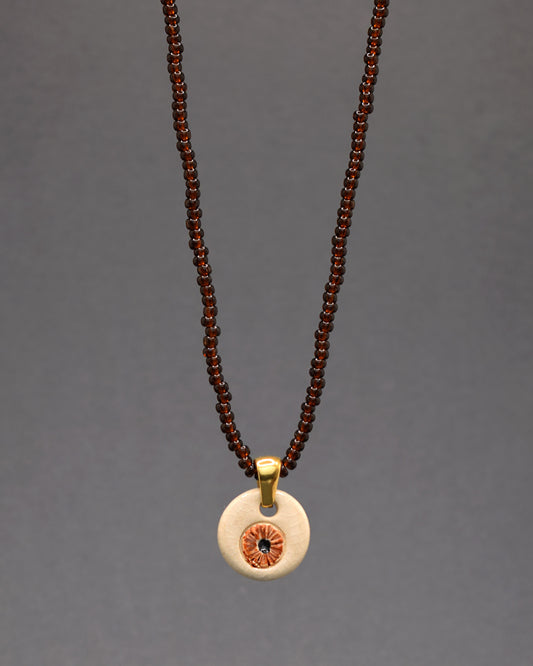 Destaque-se com o nosso pendente de cerâmica pintado à mão, apresentando um olho do mau olhado castanho, suspenso num colar de missangas de vidro semitransparentes em tons terrosos. Elegante e simbólico, este colar combina arte e proteção de maneira única, expressando estilo com significado.