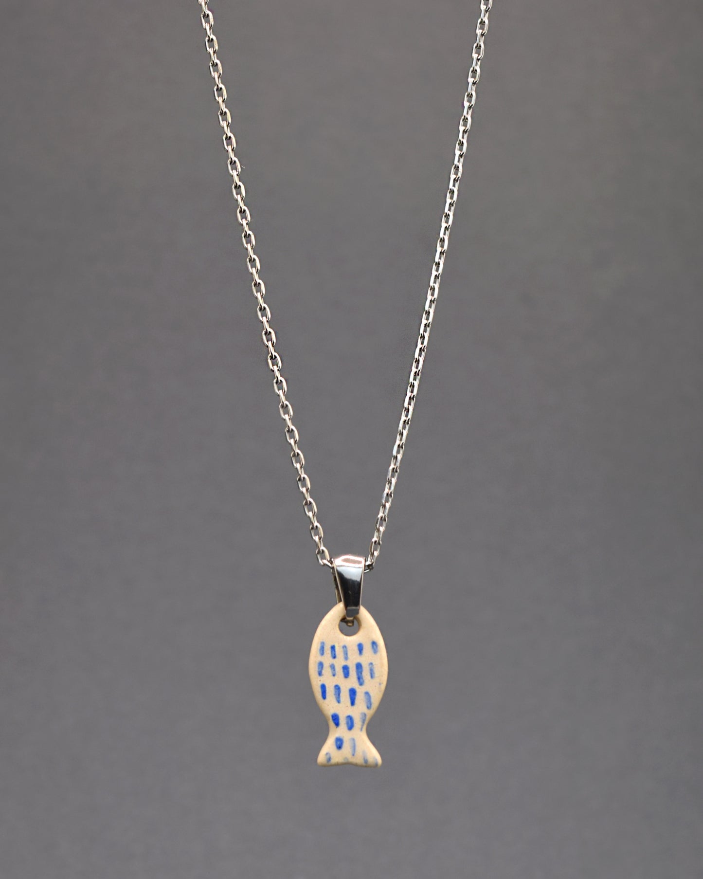 Colar em aço inoxidável com pendente de peixe em cerâmica, pintado à mão com delicadas pinceladas em azul, remetendo às escamas. Uma peça única que combina durabilidade com arte artesanal.