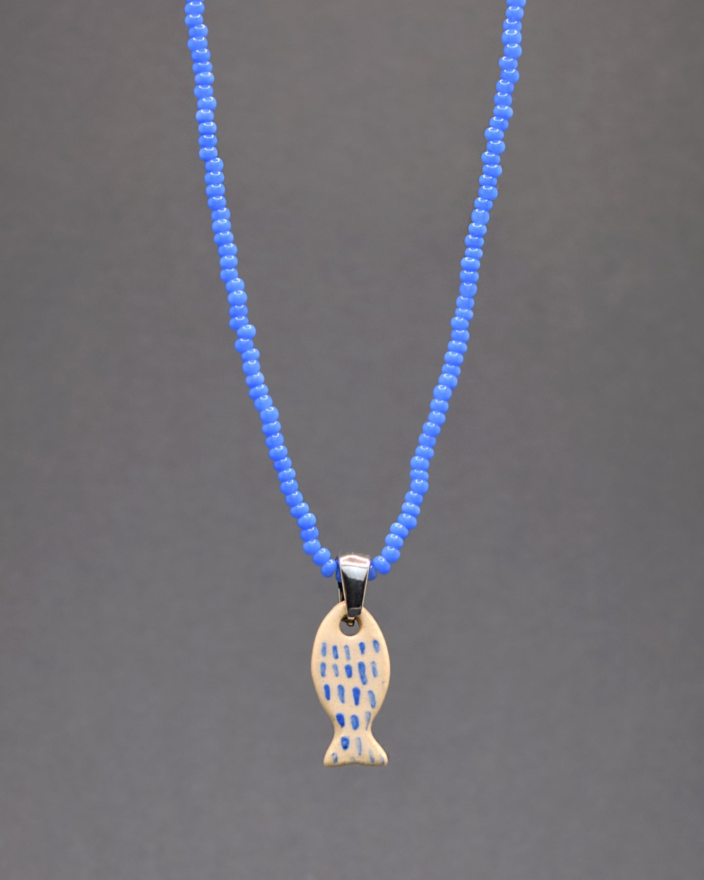 Colar vibrante com missangas de vidro azul neon, destacando um peixe em cerâmica pintado à mão. As pinceladas em azul evocam a textura das escamas, conferindo um toque artístico e um brilho único a esta peça encantadora e cheia de personalidade.