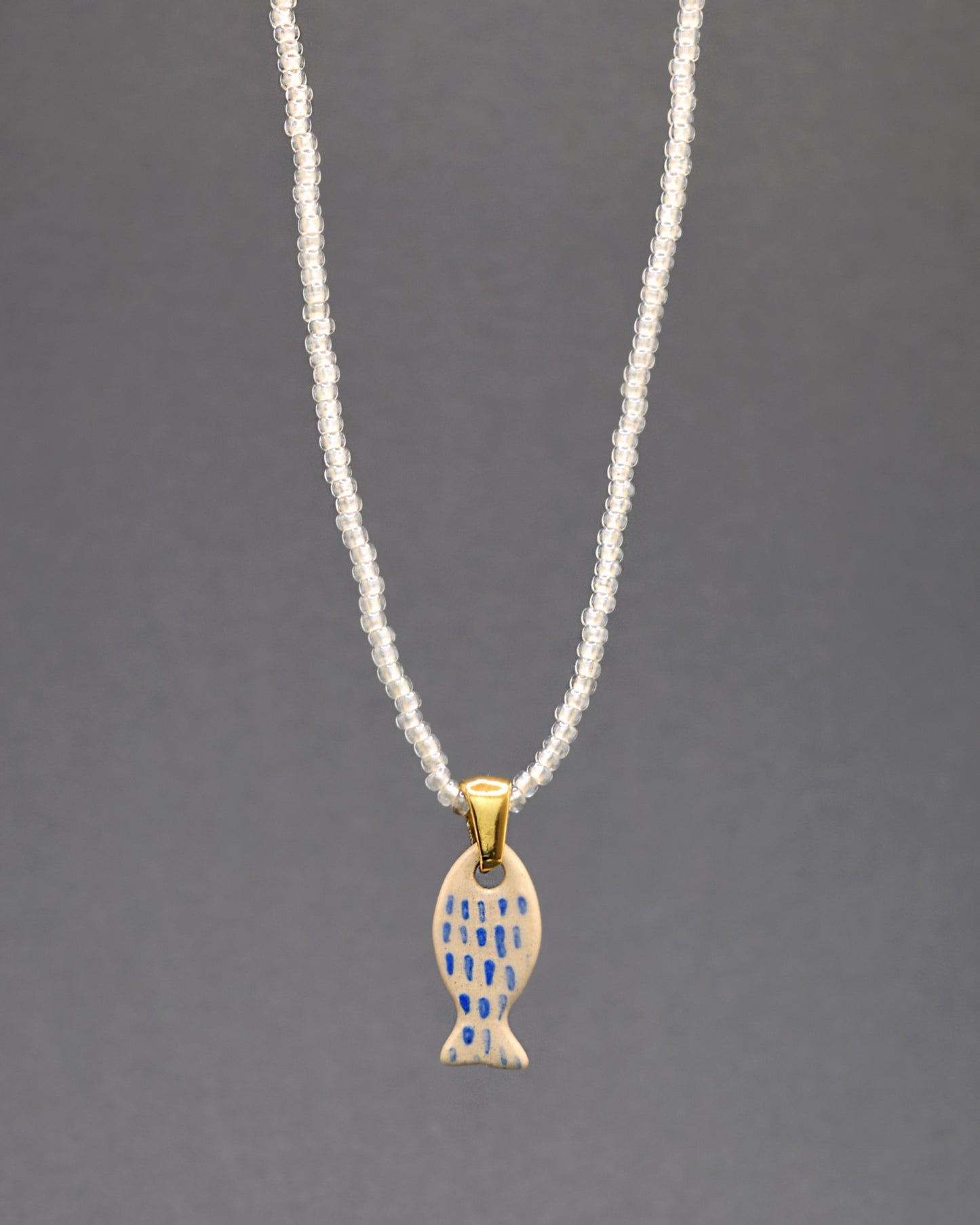 Colar delicado com missangas brancas semitransparentes, destacando um peixe em cerâmica pintado à mão. As pinceladas em azul evocam a graciosidade das escamas, conferindo um toque de sofisticação a esta peça artesanal única. Um símbolo de elegância inspirada na natureza.