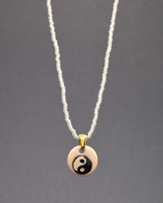 Colar delicado e etéreo: missangas brancas semitransparentes formam uma corrente leve e graciosa. O pendente de cerâmica, feito à mão, exibe o símbolo do Yin Yang em fundo branco, conferindo uma elegância sutil e equilíbrio à peça. Um acessório encantador que combina simplicidade e artesanato distintivo.