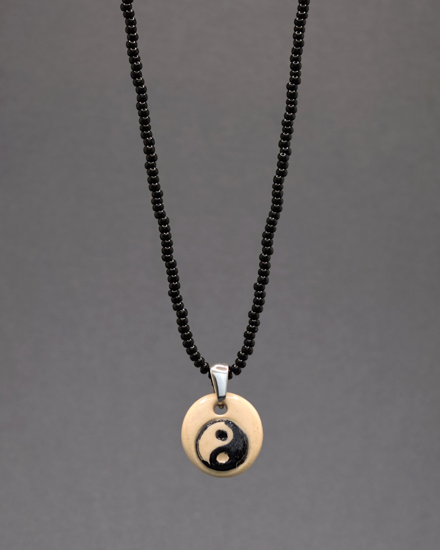 Colar intrigante e moderno: missangas de vidro pretas compõem uma corrente cativante. O pendente de cerâmica, habilmente feito à mão, exibe o símbolo do Yin Yang em fundo branco, unindo a sofisticação do preto com o equilíbrio simbólico. Uma peça única que mistura estilo ousado e artesanato refinado.