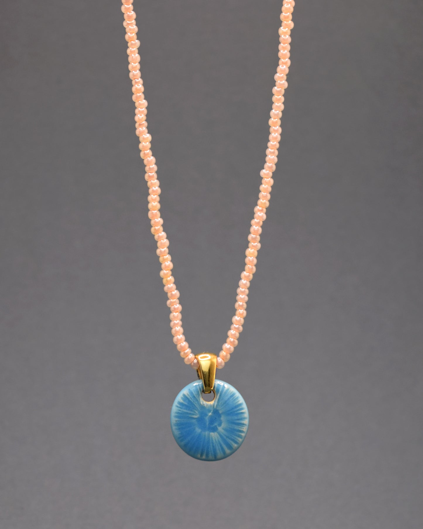 Um colar encantador de missangas de vidro salmão destaca-se pelo seu pendente de cerâmica azul celeste, modelado como uma graciosa flor do mar. A combinação de tons vibrantes de salmão e azul celeste cria uma peça de joalheria elegante e inspirada na beleza do oceano.