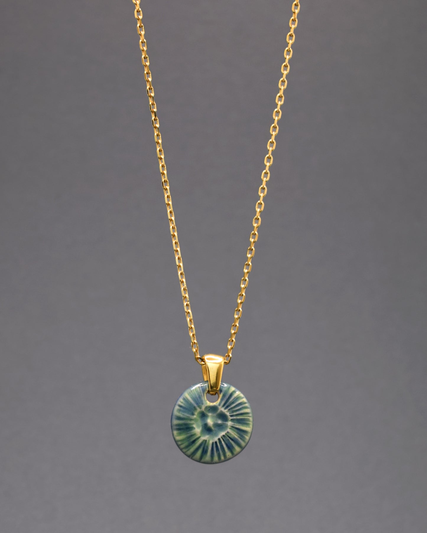 Colar deslumbrante em aço inoxidável dourado, destacando um encantador pendente de cerâmica verde musgo inspirado na beleza de uma flor do mar. A fusão do brilho luxuoso do aço dourado com a serenidade da cerâmica cria uma joia única.