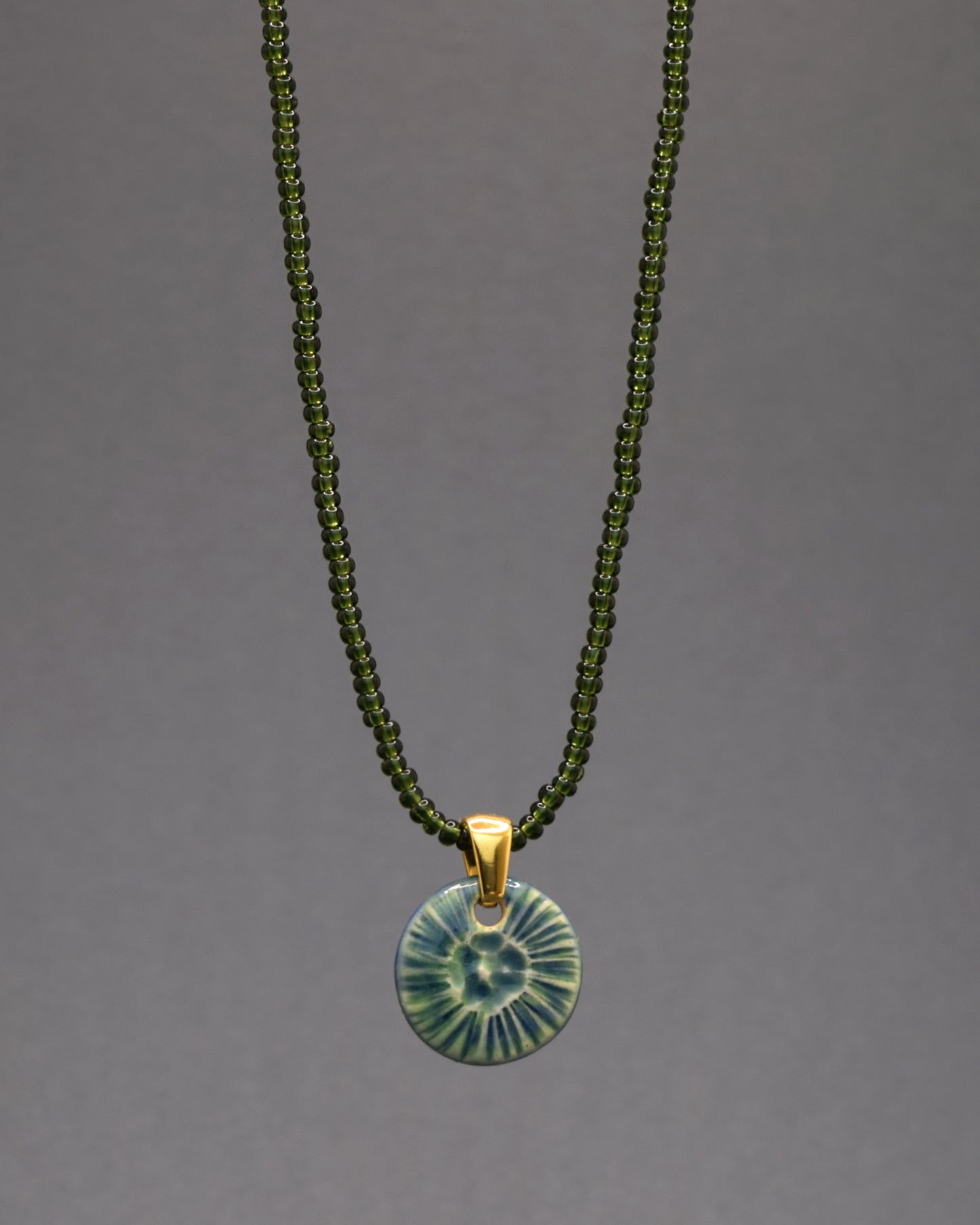 Colar fascinante com missangas de vidro verde escuro semi-transparente, acompanhado por um elegante pendente de cerâmica verde musgo inspirado na beleza natural de uma flor do mar. Uma escolha única para realçar o seu estilo de forma distinta.