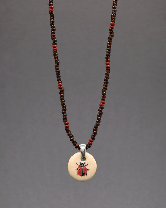 Mergulhe na elegância do nosso colar, destacando um pendente de joaninha em cerâmica pintada à mão, suspenso por missangas de vidro castanhas semitransparentes com um padrão bordô. Esta peça é uma fusão sofisticada de elementos naturais e elegância atemporal, proporcionando um charme terroso e refinado ao seu visual.