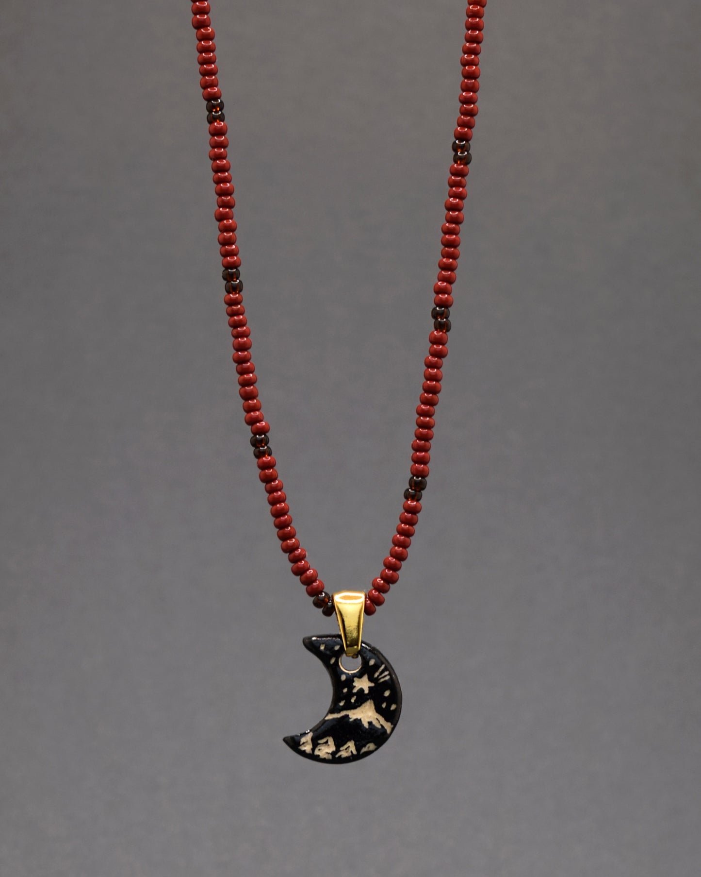 Colar envolvente de missangas bordô com padrão castanho, realçado por um pendente de cerâmica lua nova e paisagem feito à mão. Esta joia única combina riqueza de cor e artesanato delicado, proporcionando uma expressão elegante da serenidade noturna.