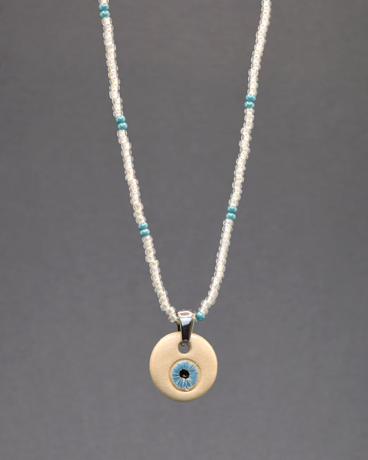 Encante-se com a sutileza do Colar Mau Olhado Olho Azul Claro, confeccionado em missangas de vidro brancas semitransparentes, com um padrão cativante em azul turquesa. O pendente de cerâmica pintado à mão destaca um olho azul, simbolizando proteção. Uma fusão de leveza e arte, este colar oferece elegância única, adicionando um toque de estilo e significado ao seu visual.