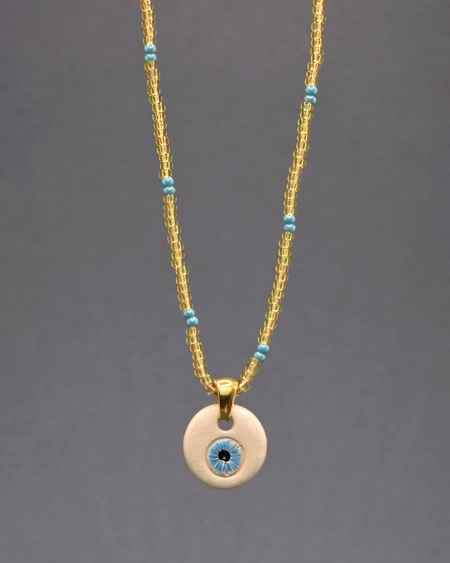 Deslumbre-se com o Colar Mau Olhado Olho Azul Claro, adornado por missangas de vidro douradas semitransparentes, com um intrigante padrão em azul turquesa. O pendente de cerâmica pintado à mão exibe um olho azul, símbolo de proteção. Uma fusão de luxo e arte, esta peça oferece um toque de sofisticação e significado único, elevando sua elegância com estilo e autenticidade.