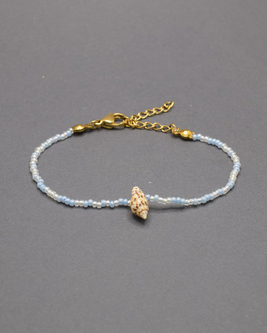 Pulseira com búzio natural e missangas de vidro em tons de azul claro, delicada e luminosa, trazendo um toque fresco e autêntico ao teu estilo.