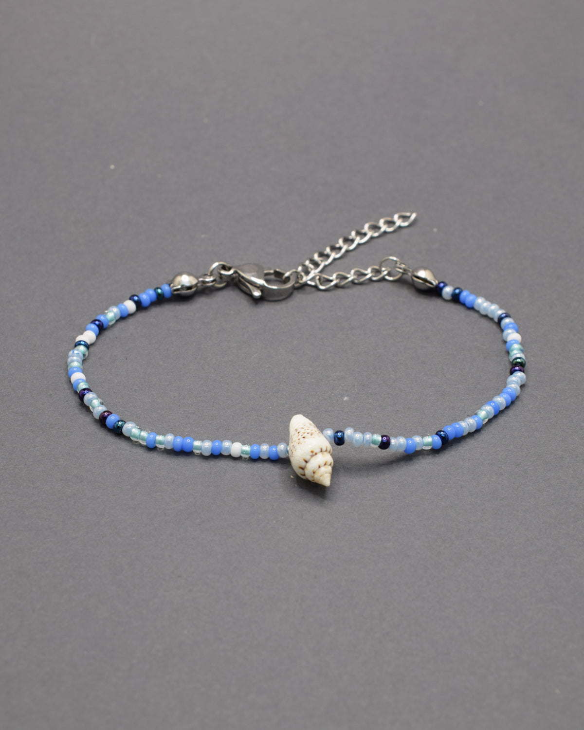 Pulseira com búzio natural e missangas de vidro em azul profundo, moderna e marcante, perfeita para um estilo autêntico com destaque subtil.