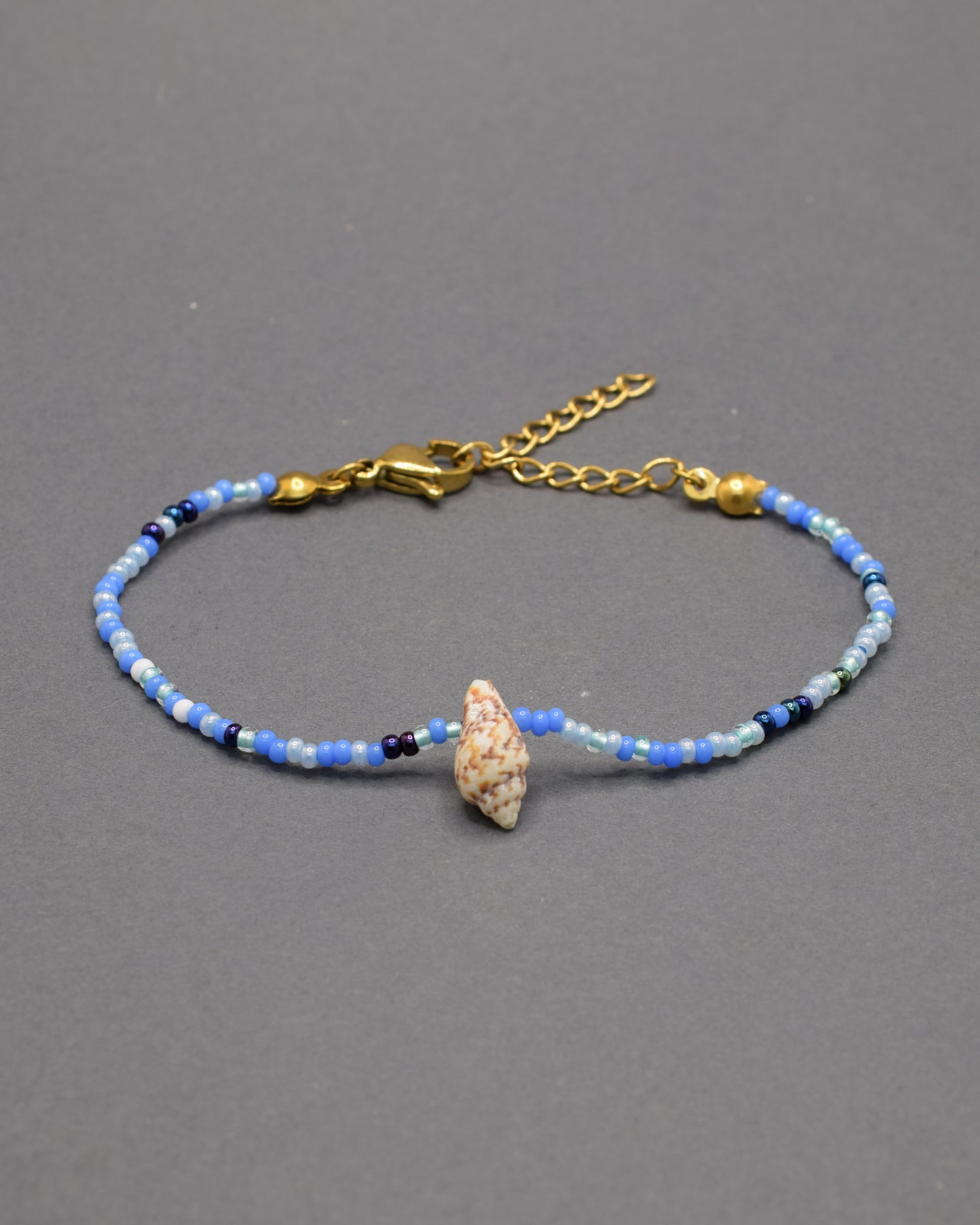 Pulseira com búzio natural e missangas de vidro em azul profundo, moderna e marcante, perfeita para um estilo autêntico com destaque subtil.