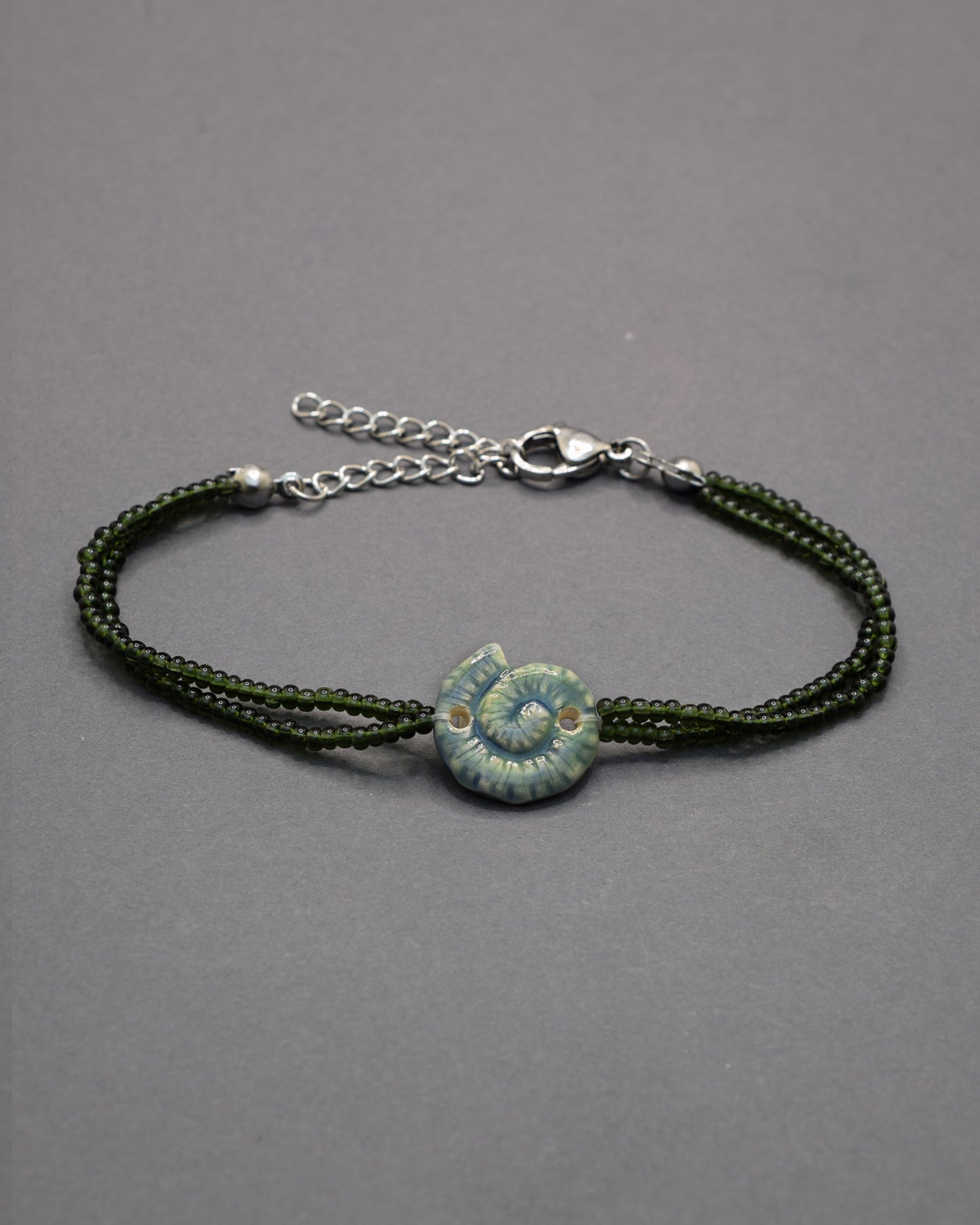 Pulseira com pendente de cerâmica caracol verde musgo, delicada e natural, perfeita para um toque original e elegante no teu look diário.