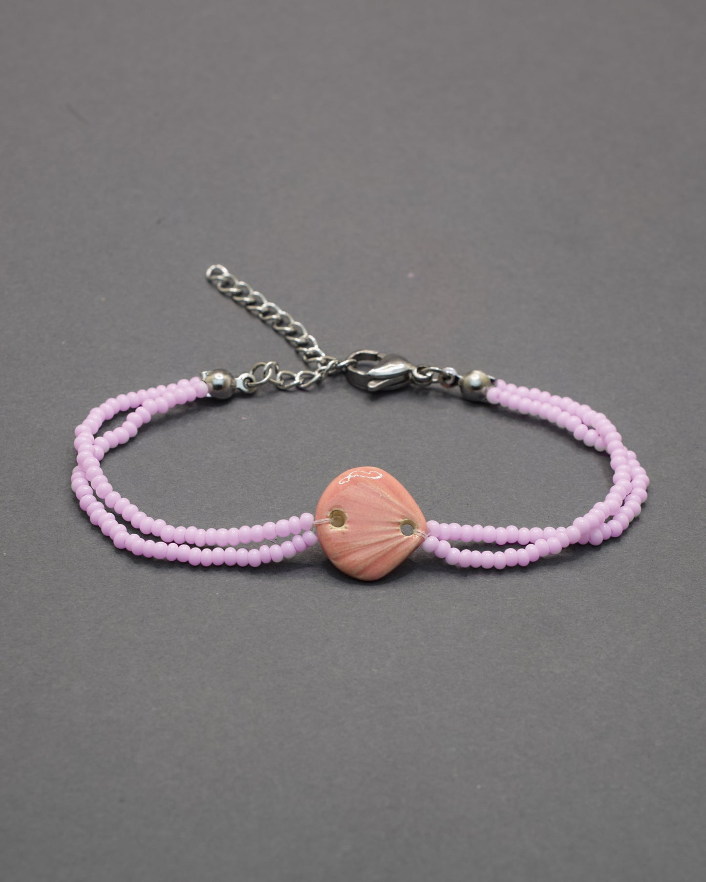 Pulseira delicada com pendente de concha rosa em cerâmica, leve e charmosa, perfeita para dar um toque praiano e elegante ao seu look.