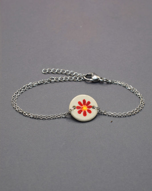 Pulseira delicada com pendente em cerâmica de margarida vermelha, vibrante e elegante, perfeita para dar um toque de cor e personalidade ao seu visual.