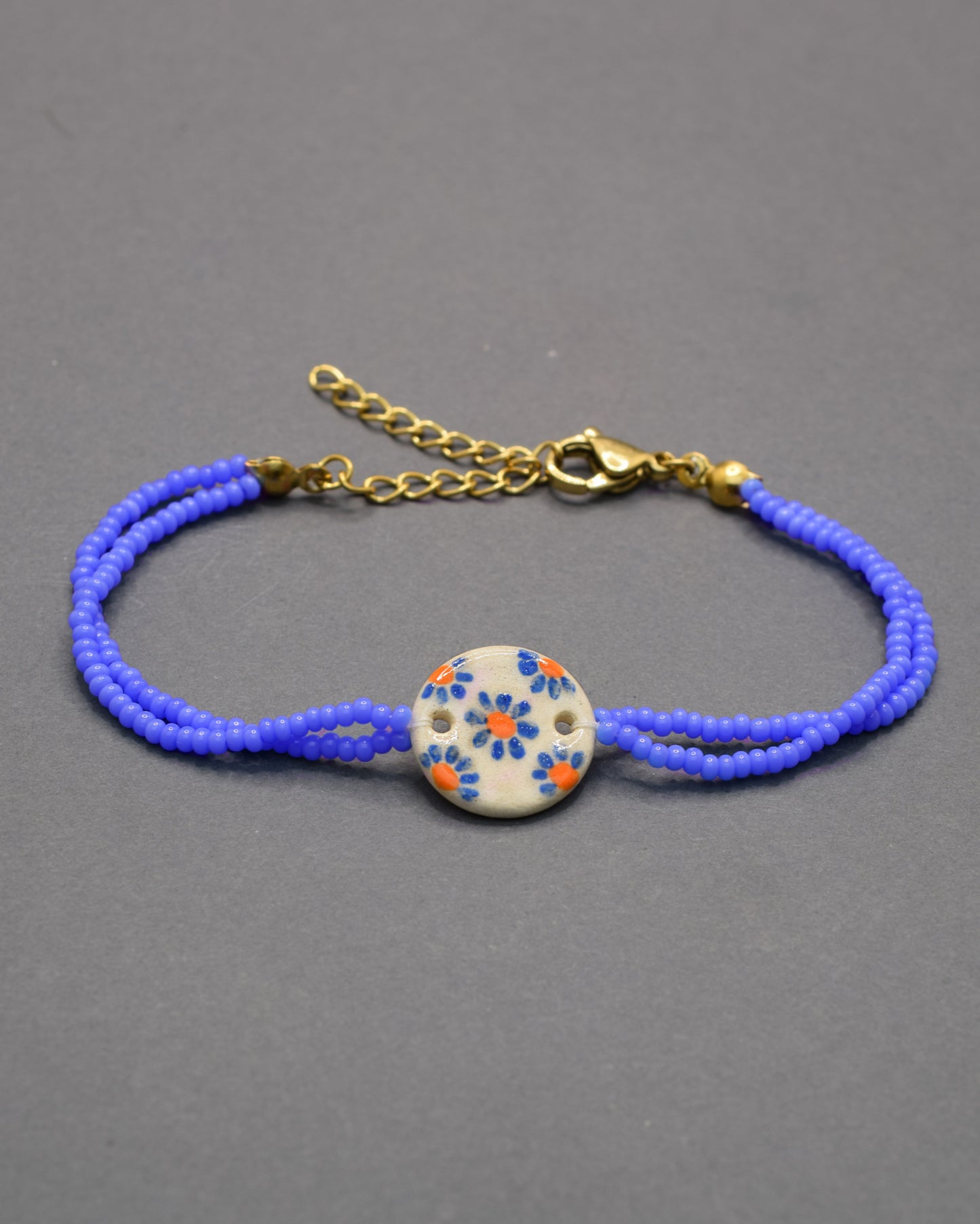 Pulseira delicada com pendente em cerâmica de margaridas azuis, leve e romântica, perfeita para dar um toque floral e encantador ao seu visual.